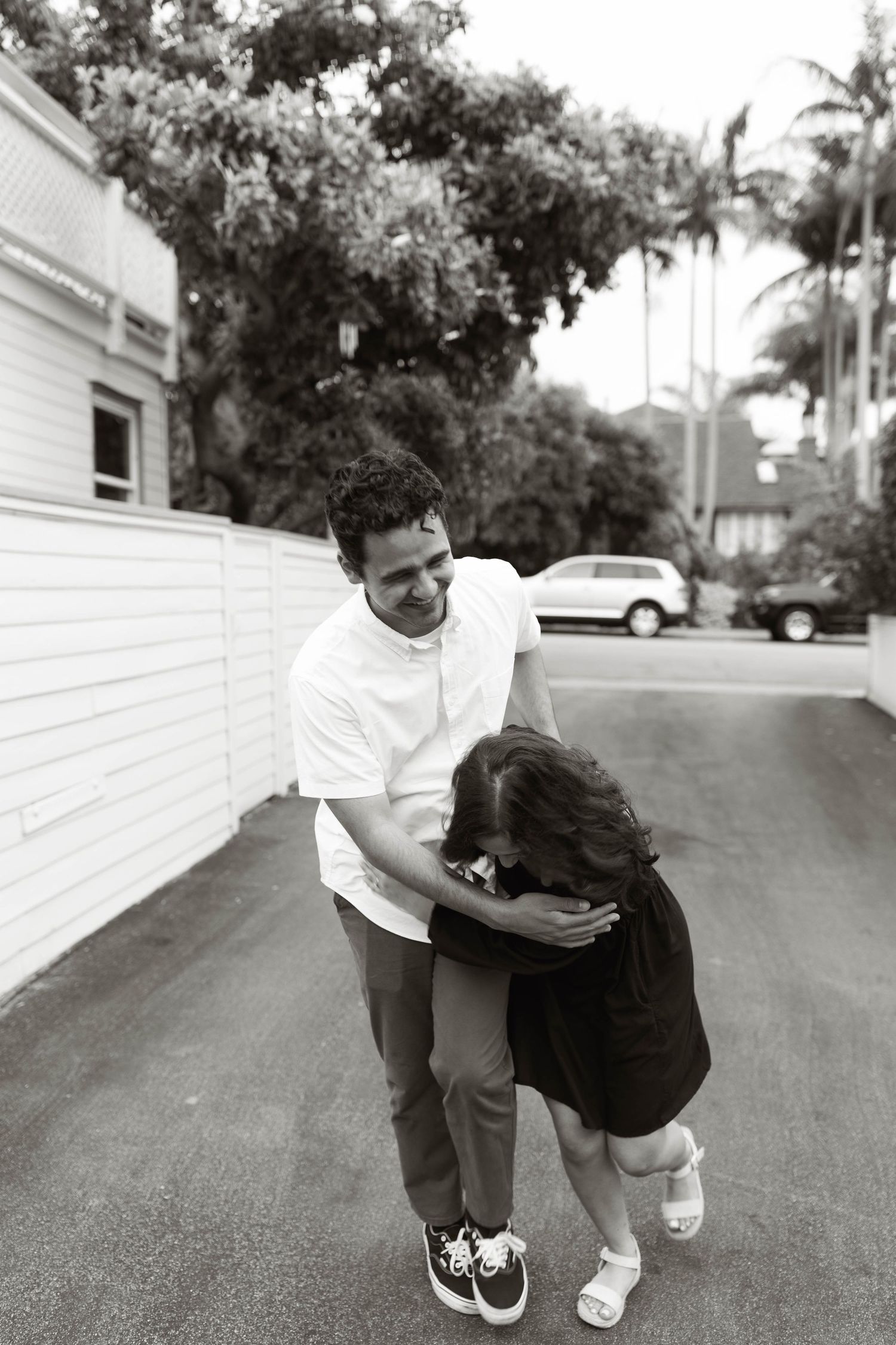 Black and white photo sequence of two people playfully interacting on a suburban street.
