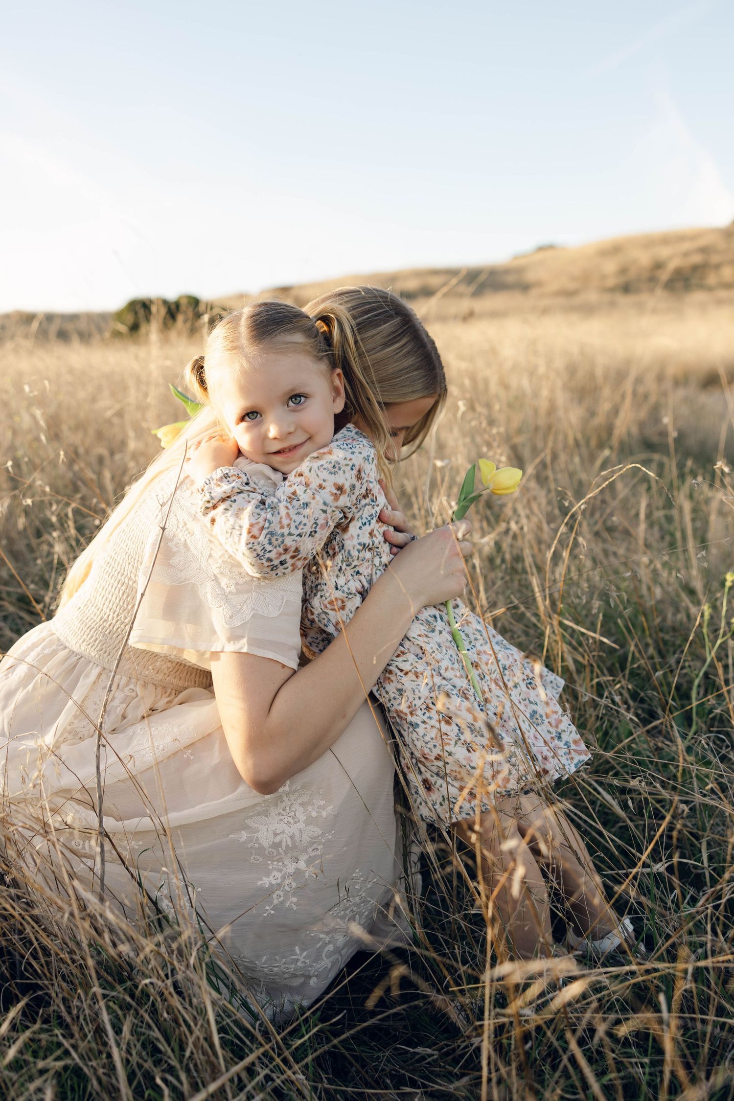 Mother and daughter sharing intimate embrace in sunlit field during golden hour.