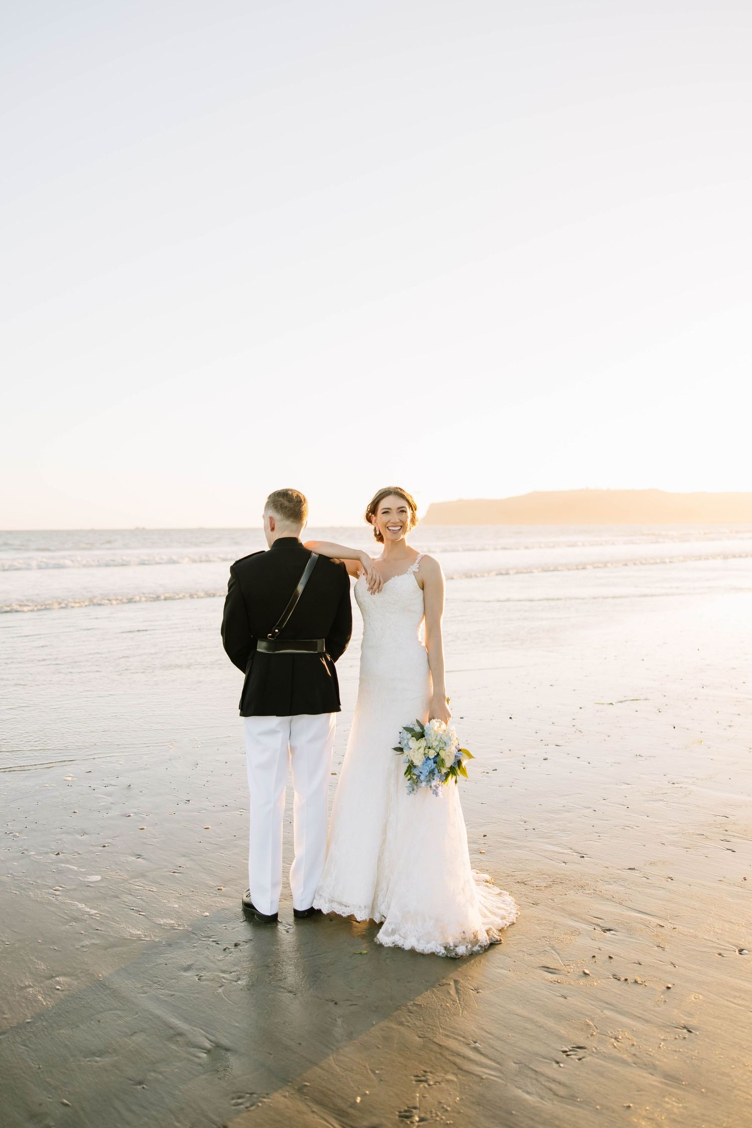 Wedding ceremony on sandy beach at sunset with couple and officiant in white attire.