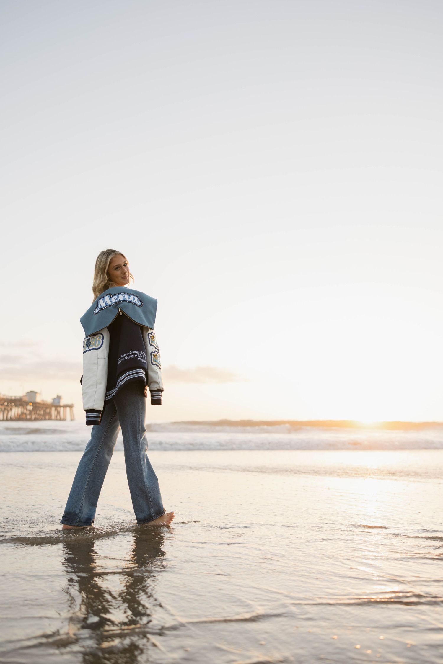 Two people stand in shallow ocean water at sunset wearing matching denim.