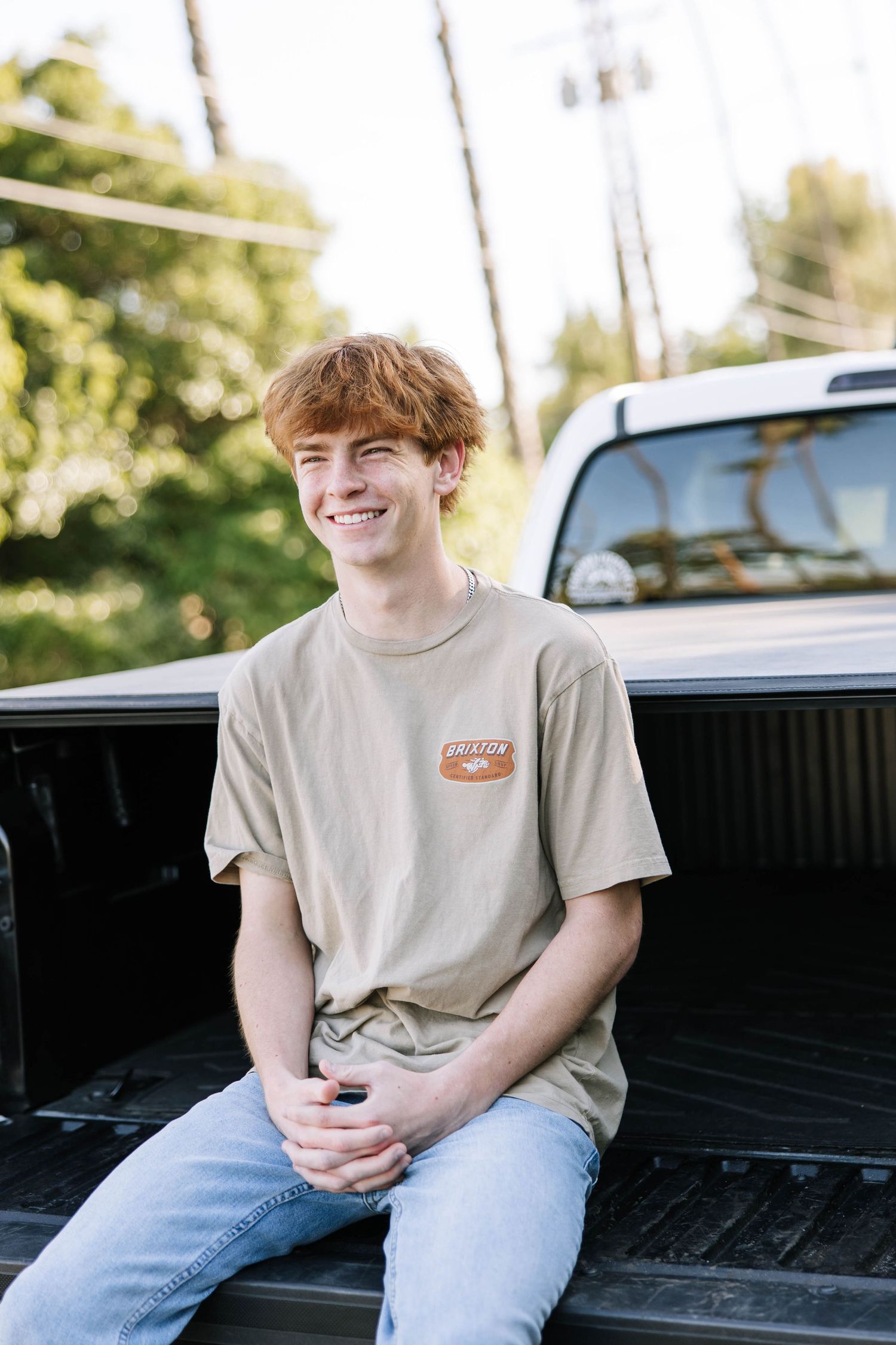 Person in gray t-shirt sitting casually in truck bed during outdoor photoshoot.