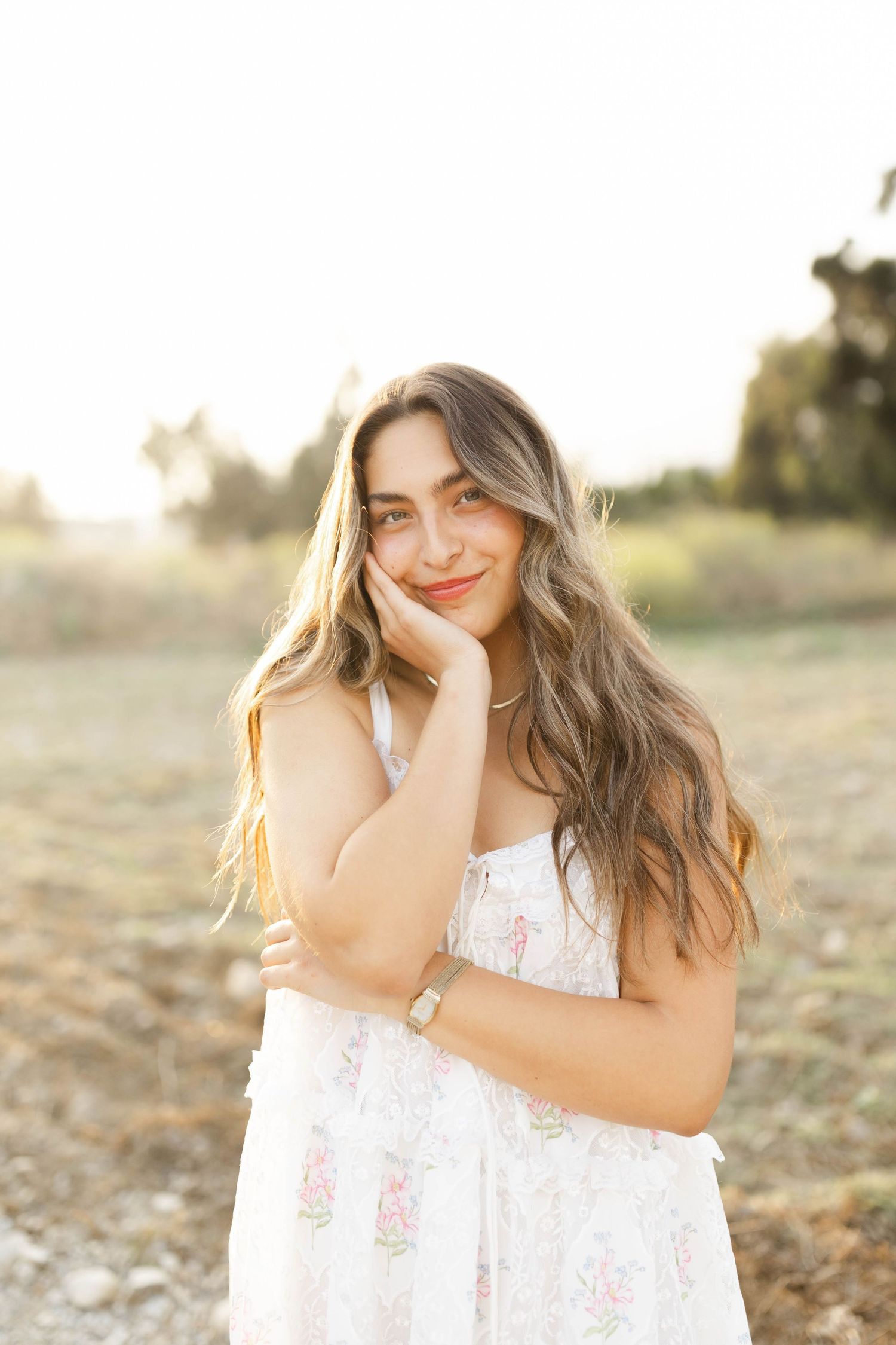 Person in white lace dress posing playfully in sunlit field at sunset.