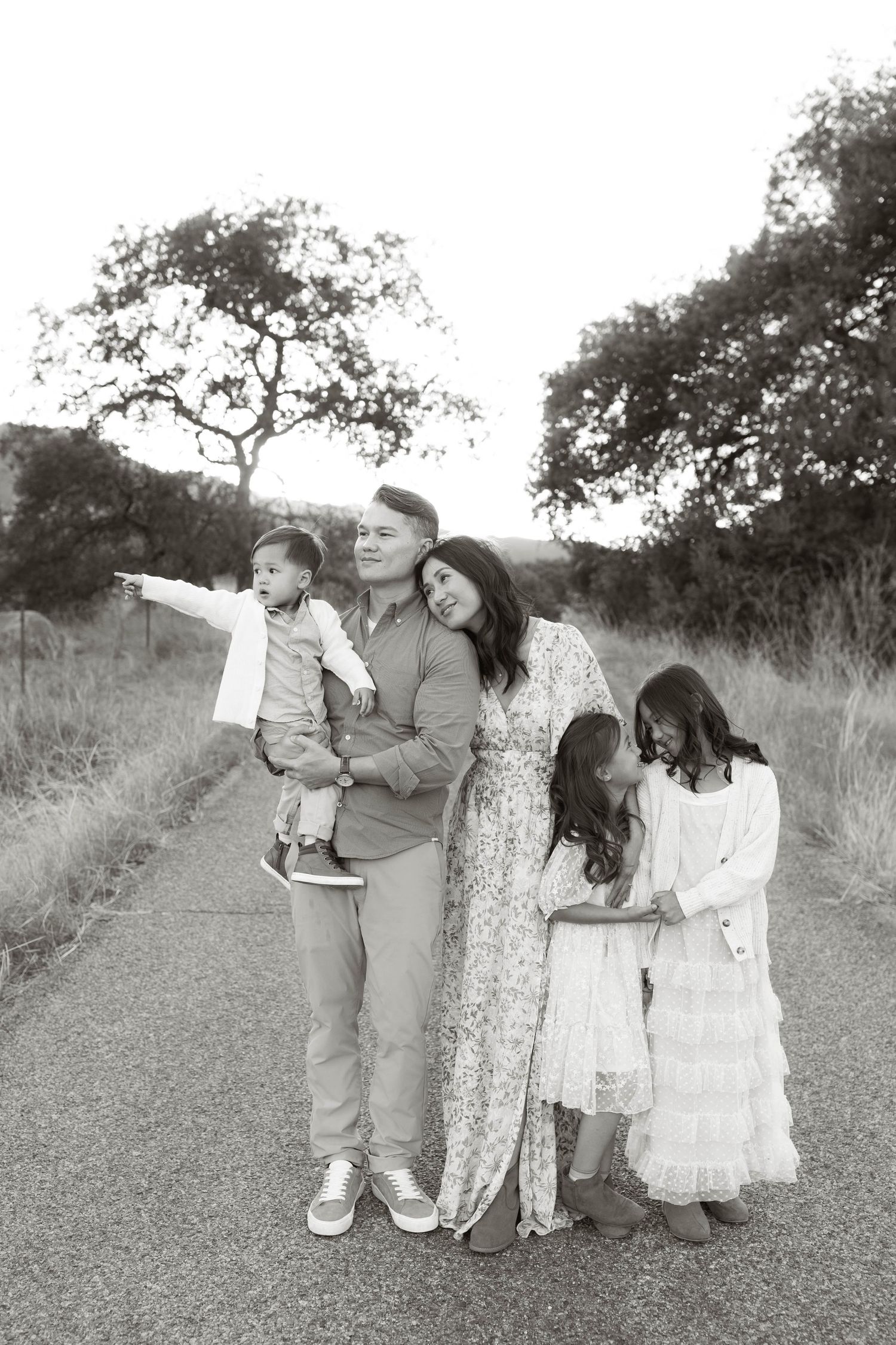 Family group portrait in casual attire standing together on a dirt path surrounded by nature.