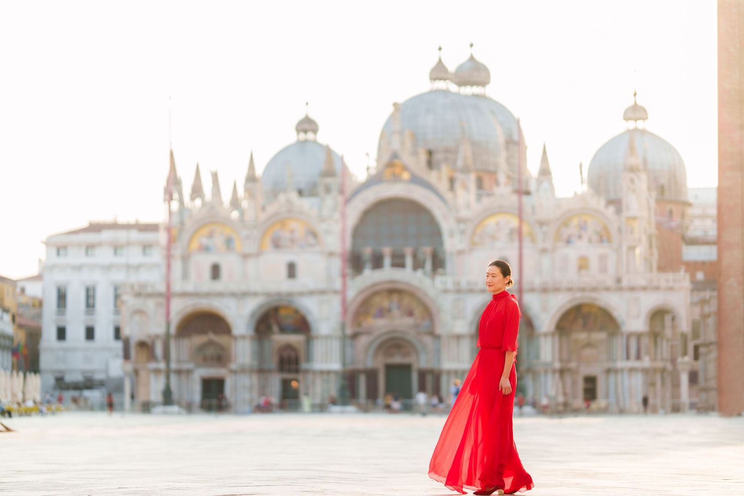 Woman in red gown walks St. Mark's Square, Venice, with the iconic Basilica di San Marco in the background.