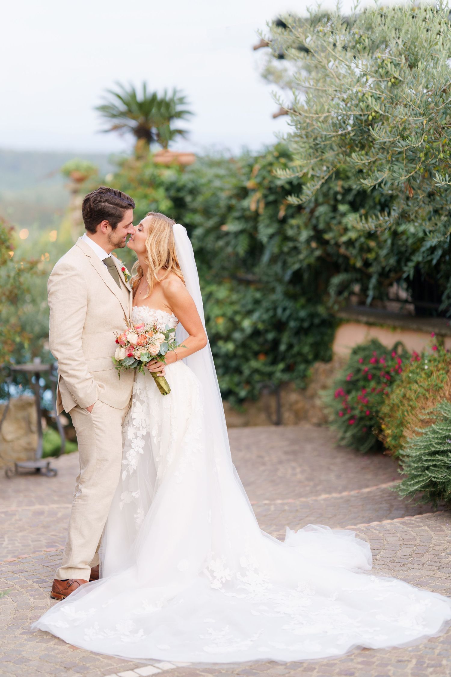 A romantic wedding couple shares a tender moment in a garden setting with lush greenery and a flowing white dress.
