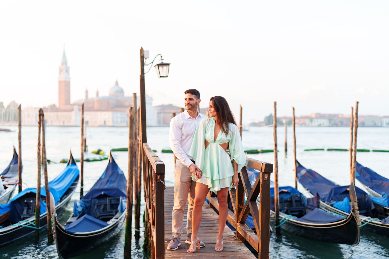 Couple enjoying romantic moment on wooden pier with traditional gondolas and Venice skyline in background.