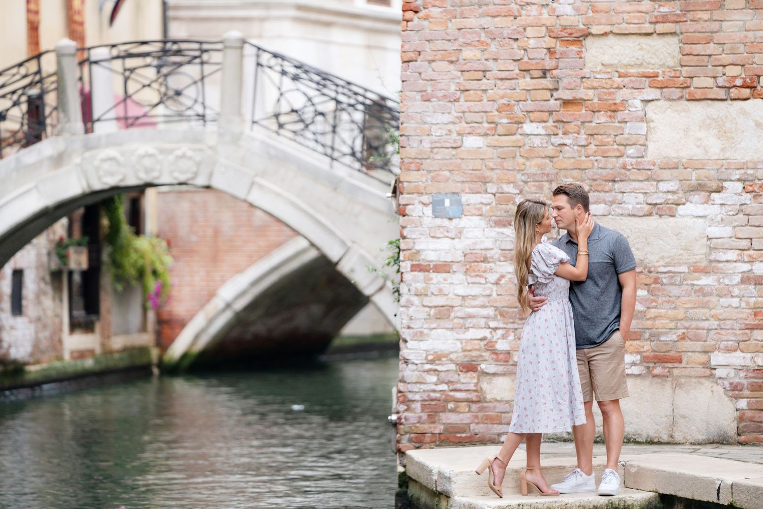 Romantic couple embraces on a charming stone bridge over a Venice canal with historic architecture in the background.