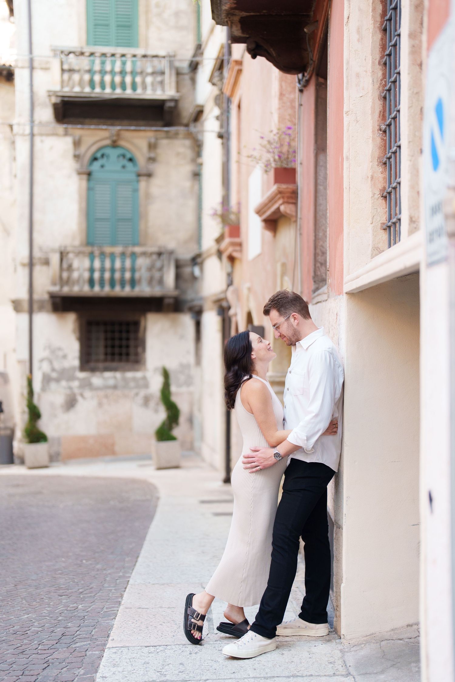 A couple shares a romantic moment against a pastel-colored wall in an old European street setting.