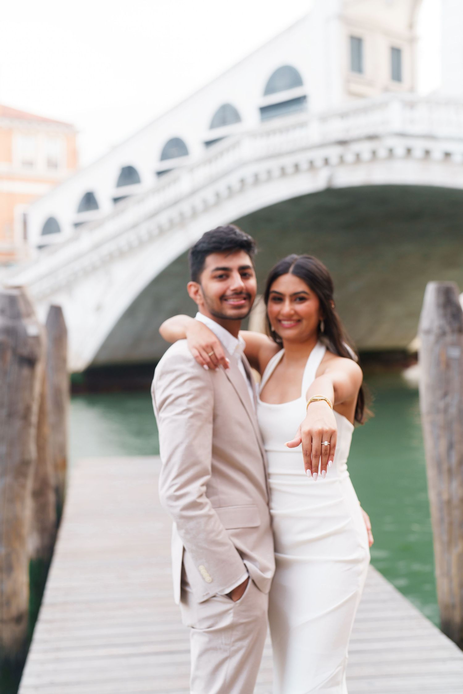 A couple shares romantic moments along Venice's canals with a historic bridge in the background.
