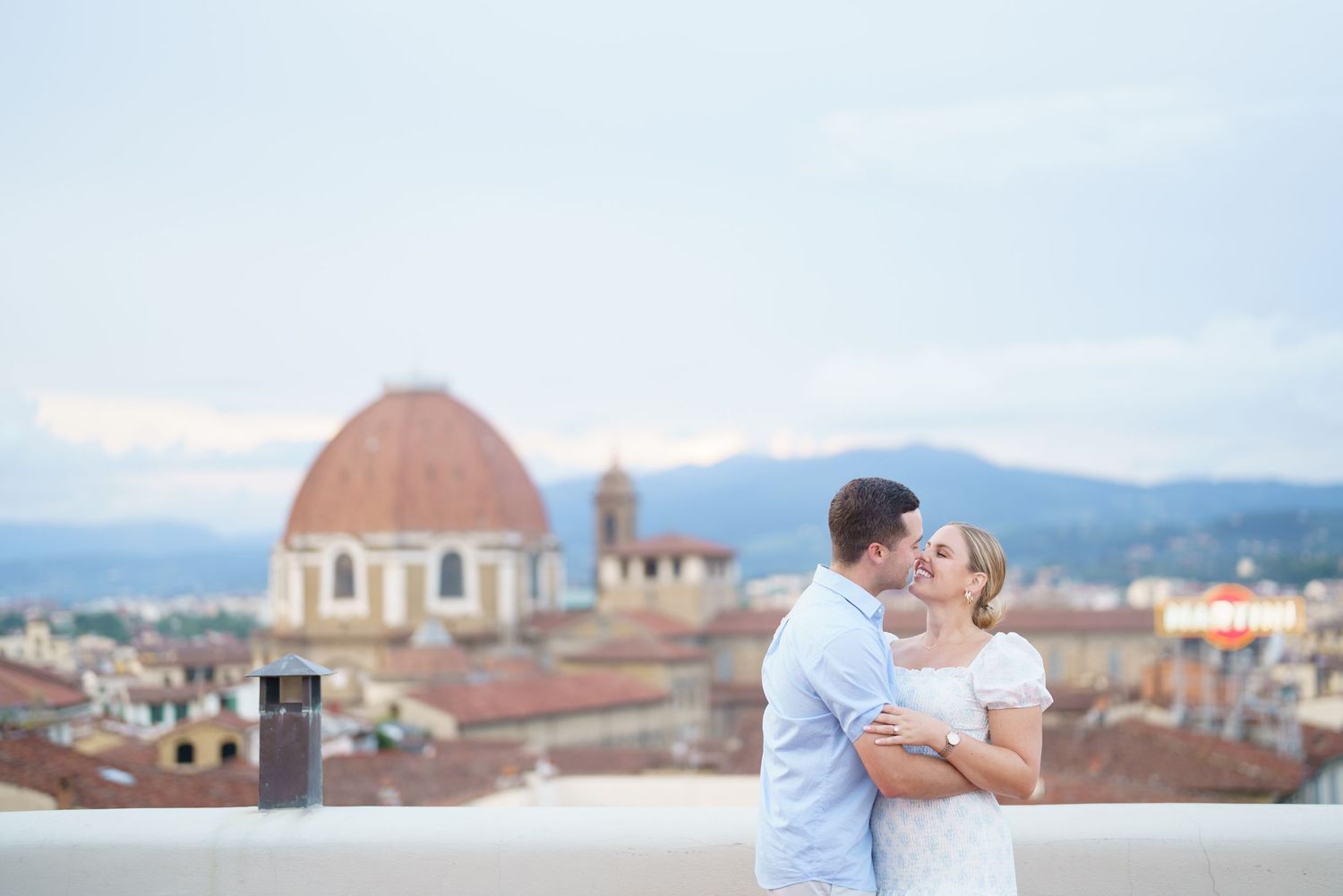 Romantic couple embraces while enjoying panoramic views of Florence, Italy with historic domed buildings in background.