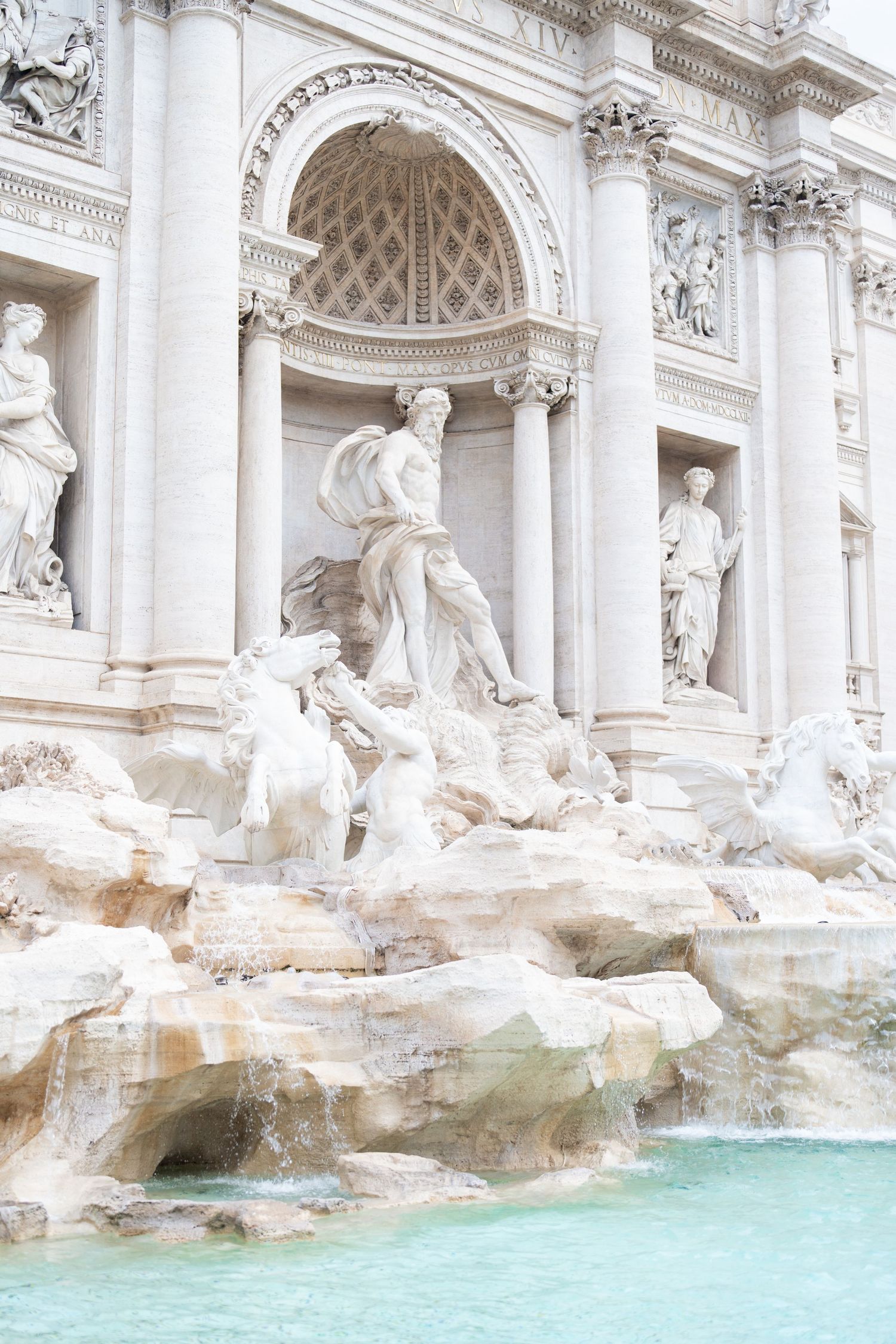Close-up architectural detail of the Trevi Fountain showing white marble sculptures and turquoise water.