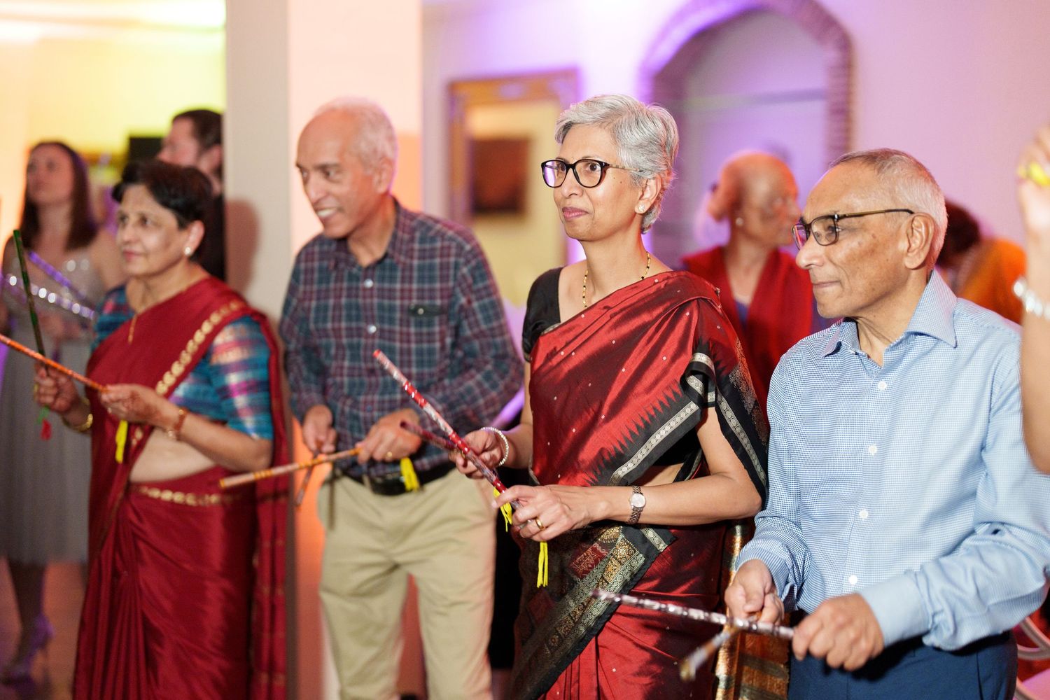 Wedding guests dancing and enjoying themselves at a reception with purple ambient lighting.