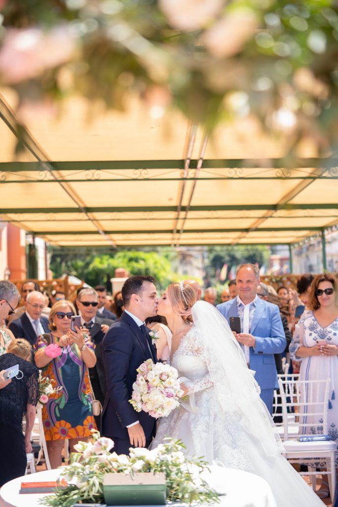 Wedding celebration under a canopy with white chairs and floral decorations.