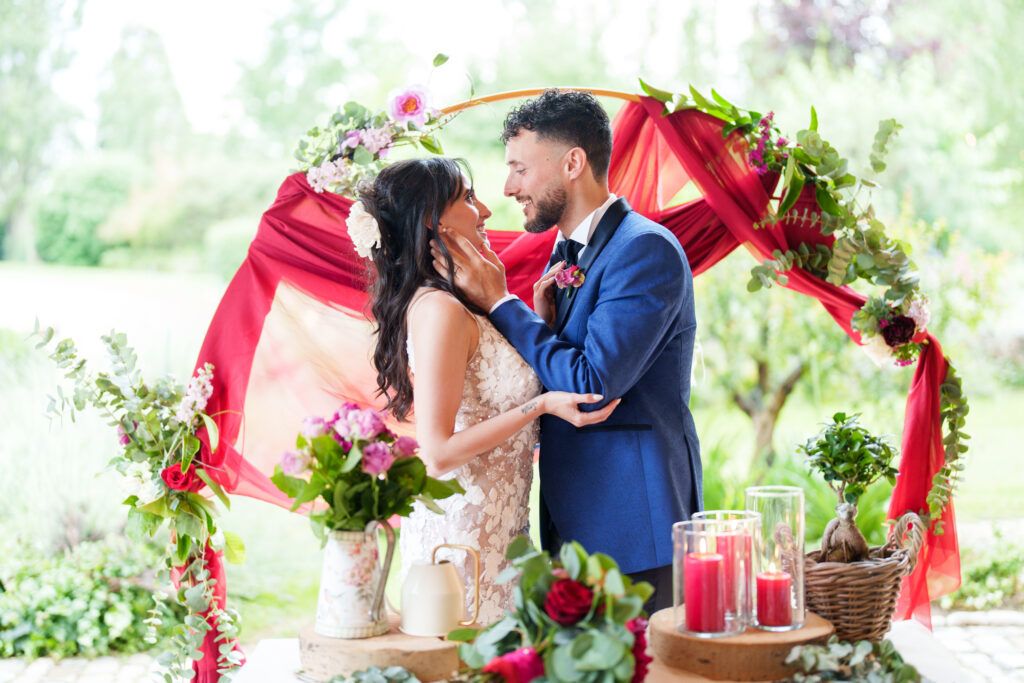 Romantic red floral arch frames intimate wedding ceremony moment.
