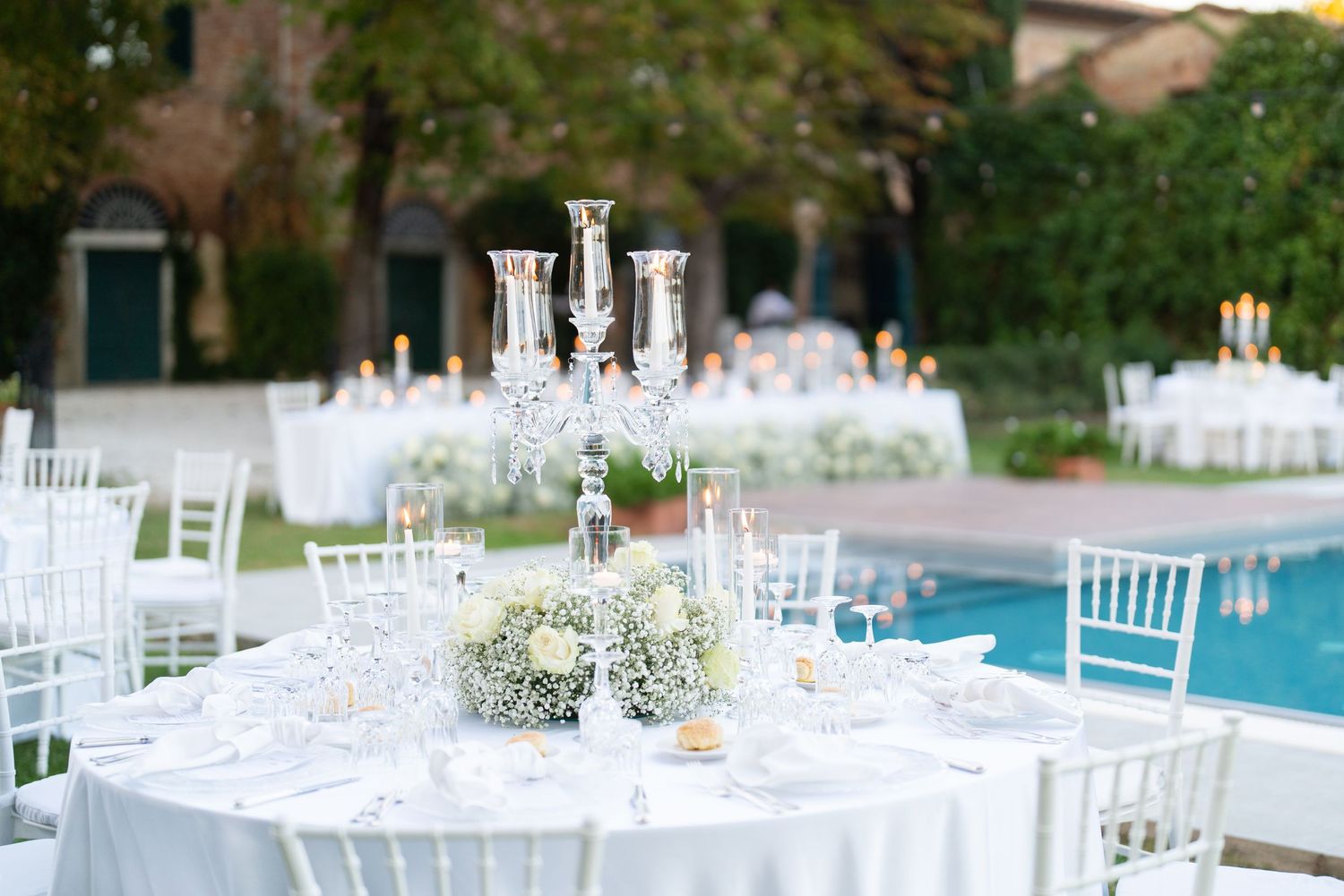 White wedding reception tables with crystal centerpieces and chiavari chairs by poolside.
