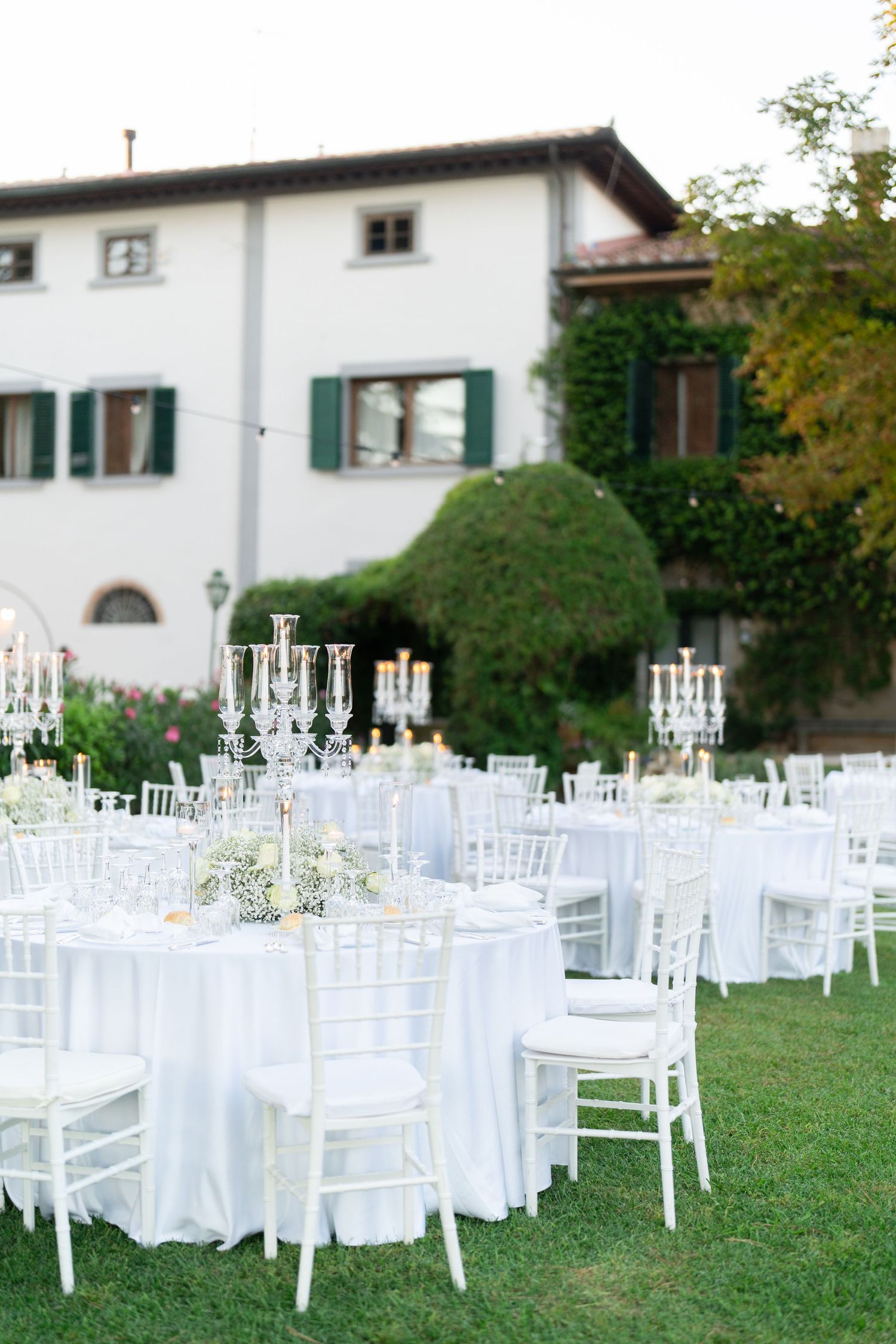 White chiavari chairs and round tables set up on a lawn for an outdoor wedding reception.