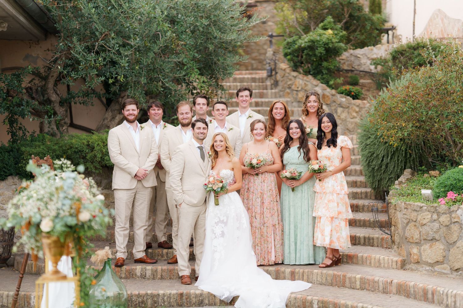 Wedding group photo with bridal party in pastel colors arranged on garden staircase.