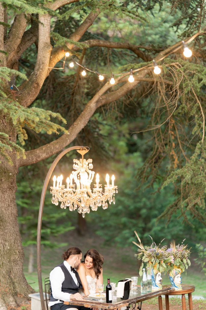 Garden wedding setup with hanging crystal chandeliers and string lights creating magical ambiance.