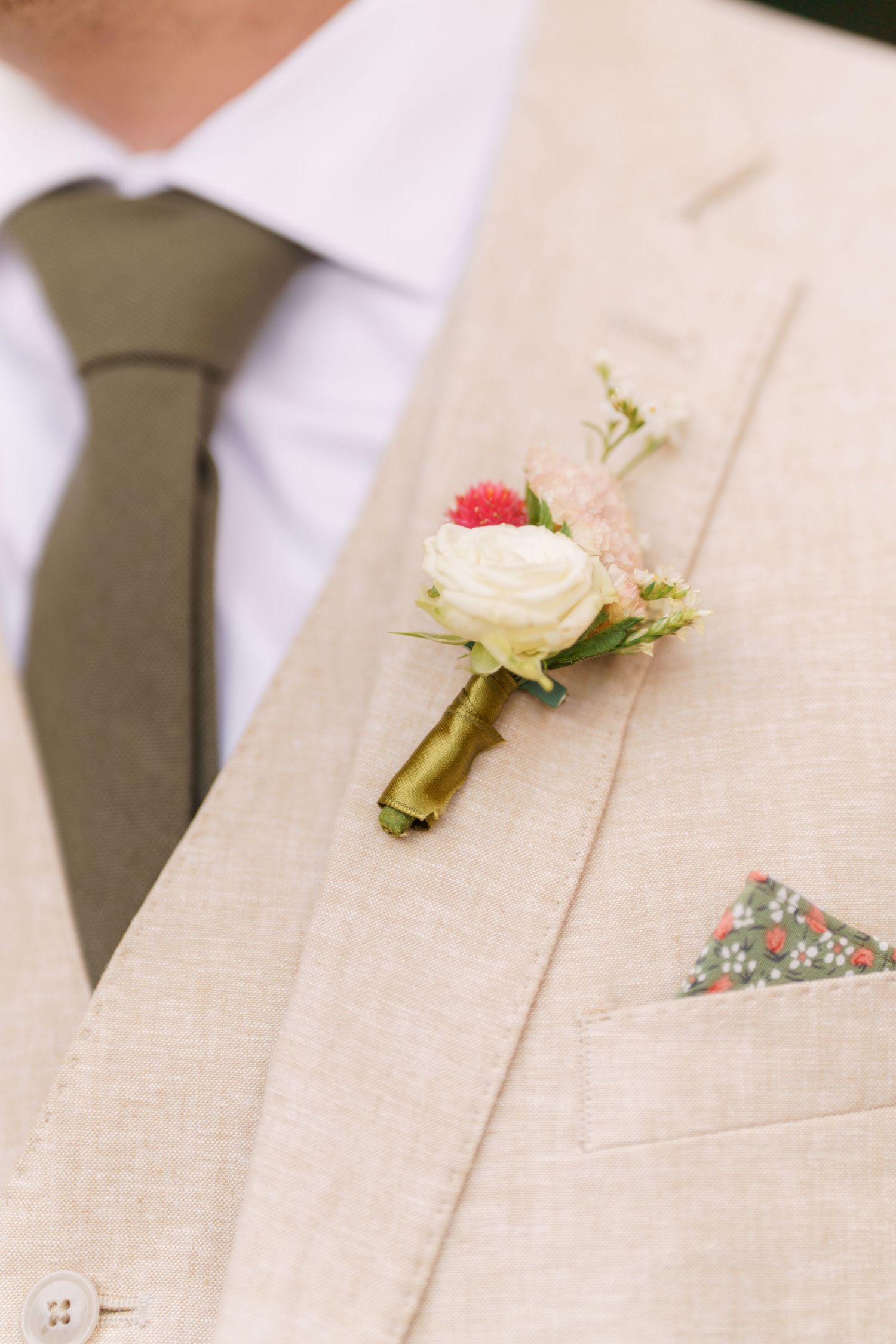 Cream colored boutonniere with white rose pinned to beige suit lapel.