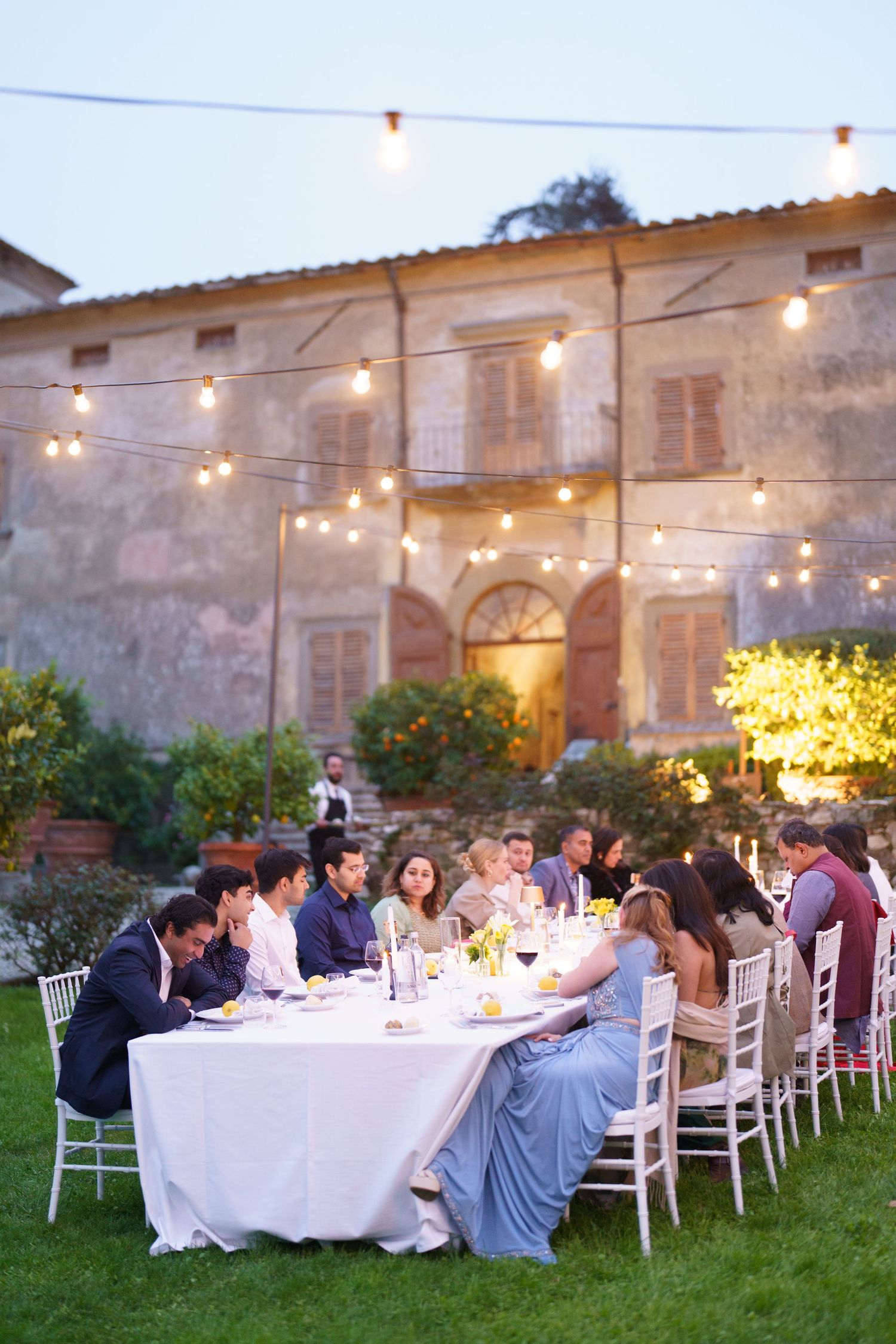 Outdoor wedding dinner setup with string lights at rustic Italian villa.