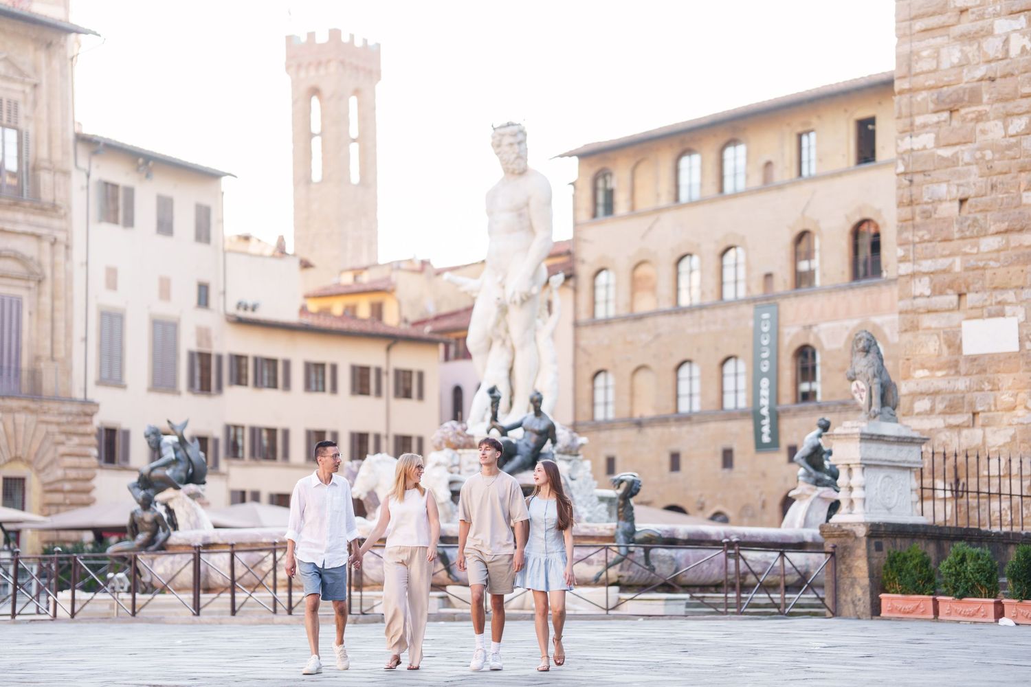 Tourists enjoying a sunny day in Piazza della Signoria, Florence, with historic buildings and statues in the background.