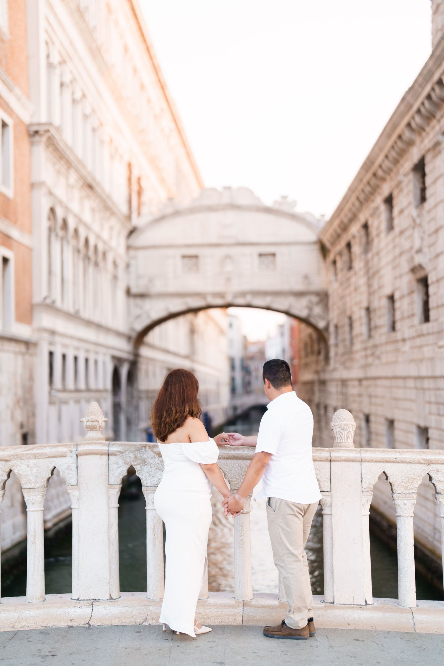 A romantic couple sits together on the Bridge of Sighs in Venice, Italy during a dreamy sunset moment.