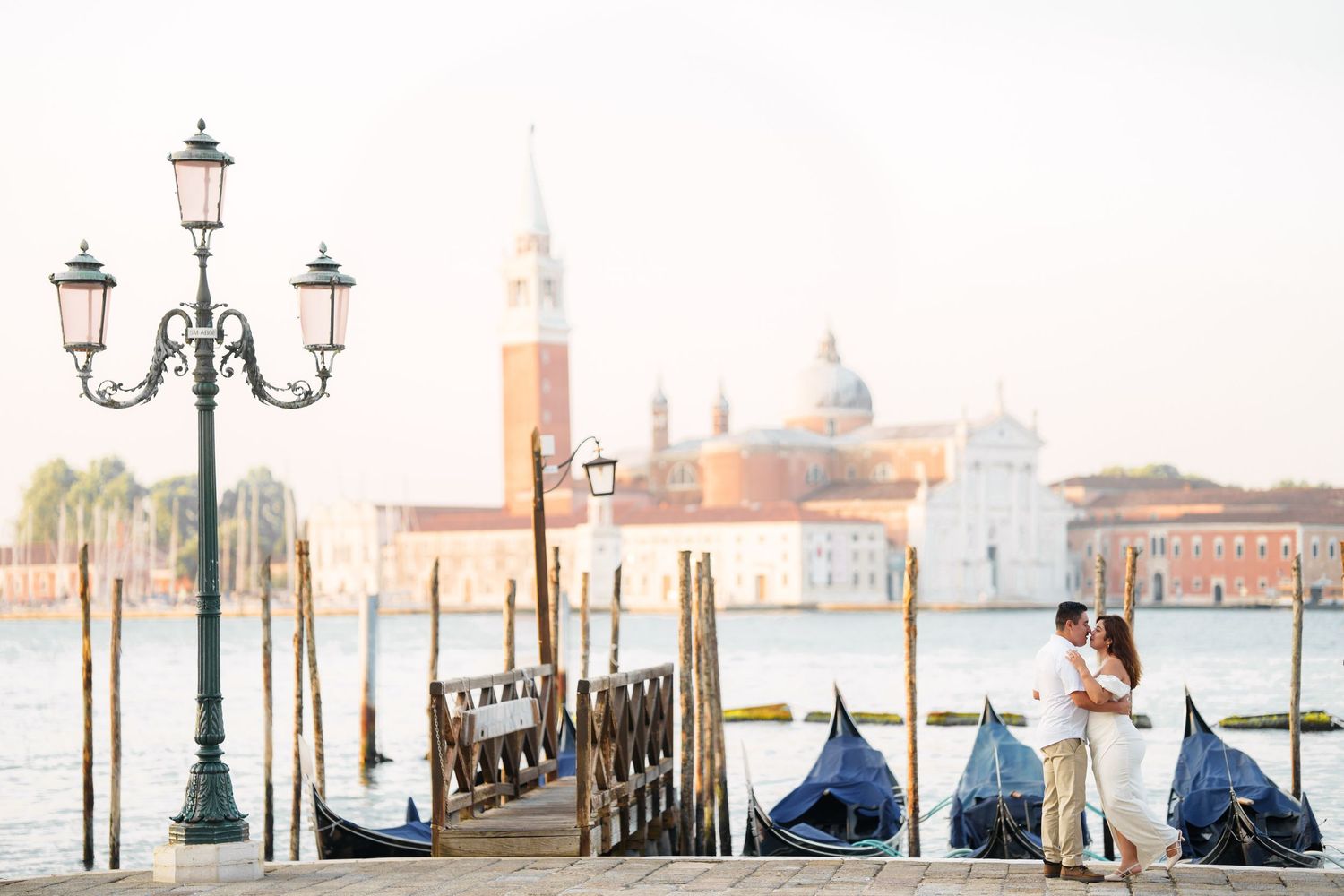 A misty morning view of Venice's Grand Canal with street lamps and covered gondolas along the waterfront.