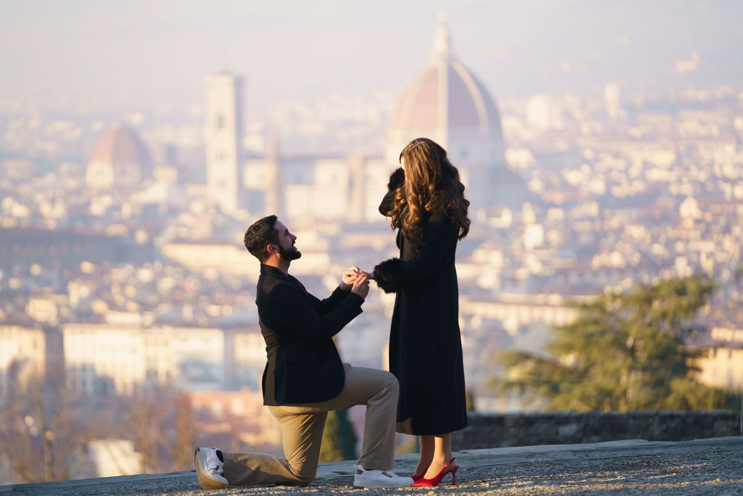 Two people enjoy a scenic sunset view overlooking a cityscape from a hilltop vantage point.