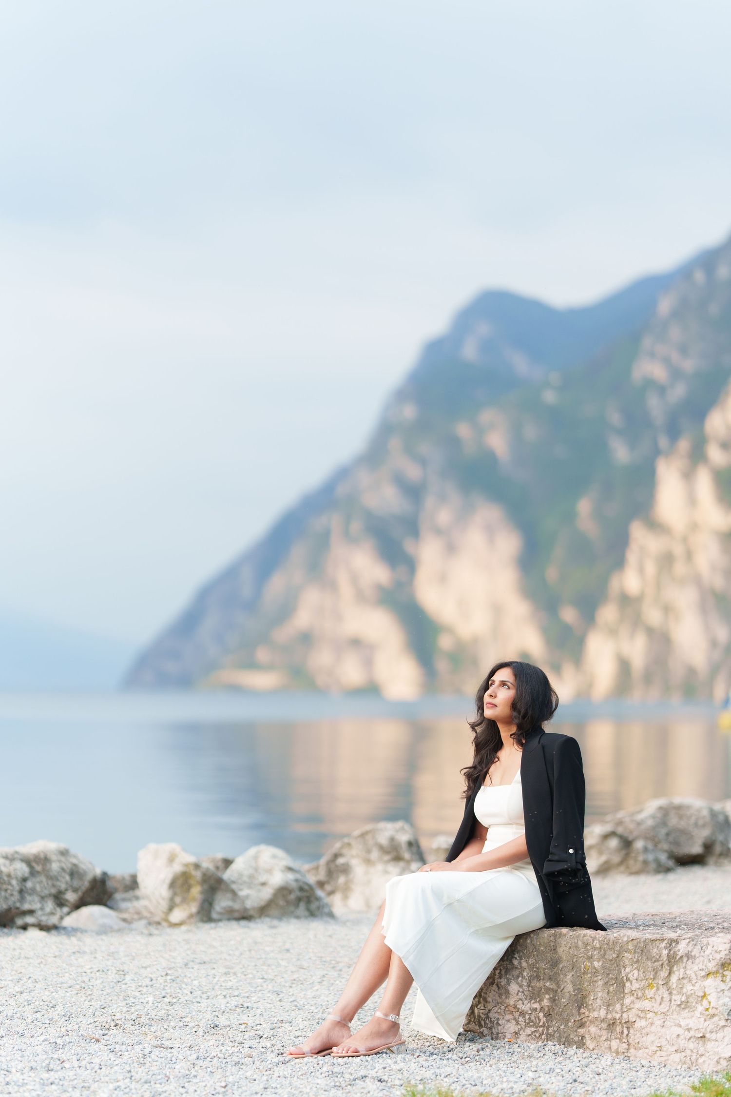 Couple sits together on rocky beach overlooking scenic mountain coastline at sunset.