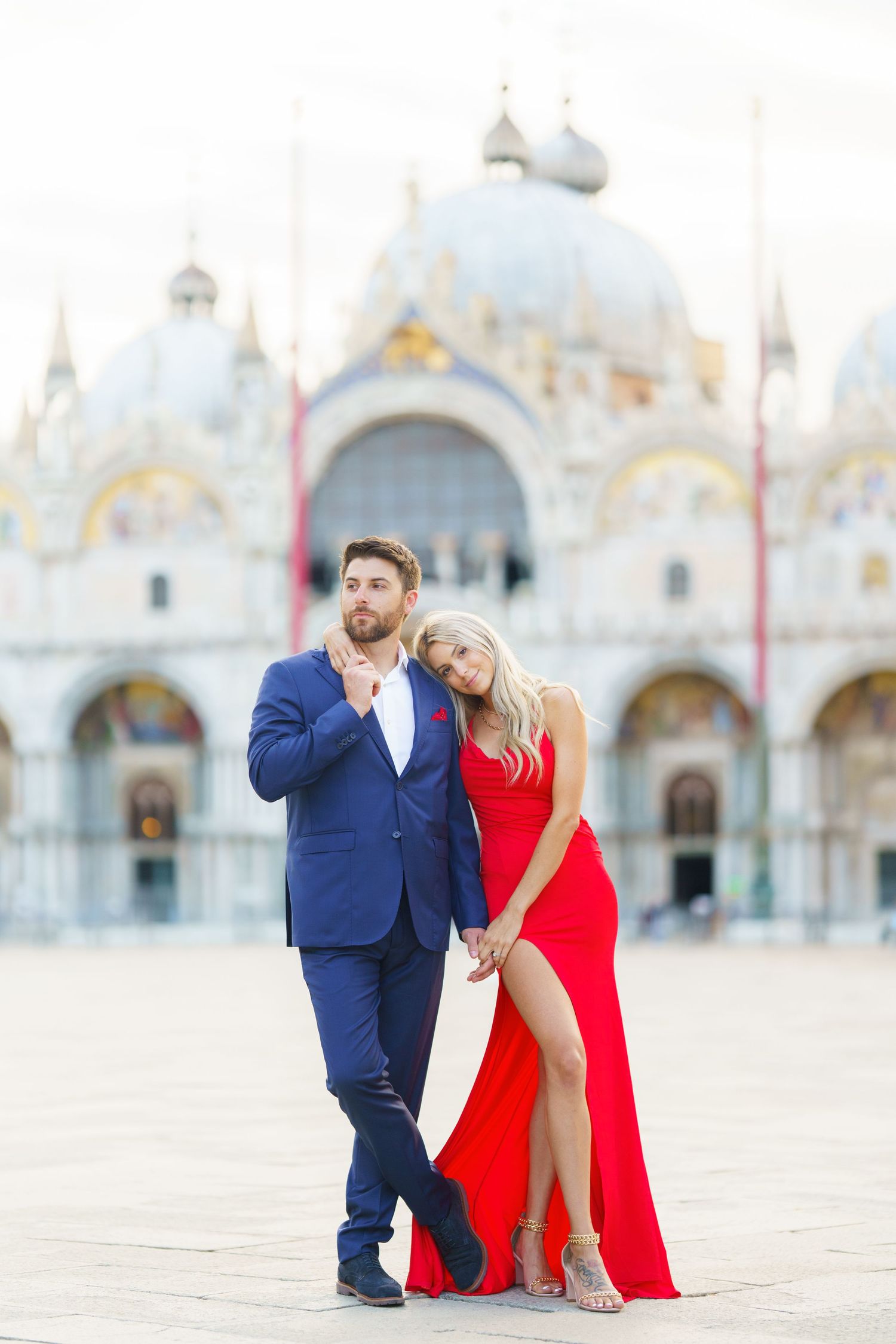 A couple poses romantically in formal attire at St. Mark's Square in Venice with the basilica in the background.