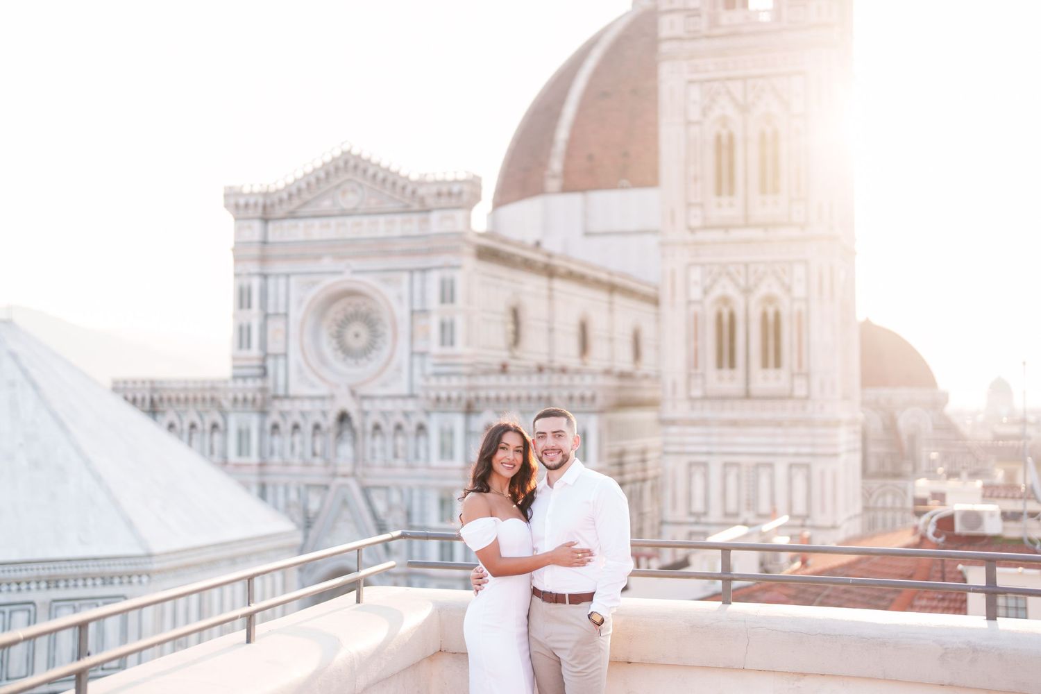 A couple embraces during a romantic sunset photoshoot on a rooftop in Florence, Italy with the Duomo cathedral visible.