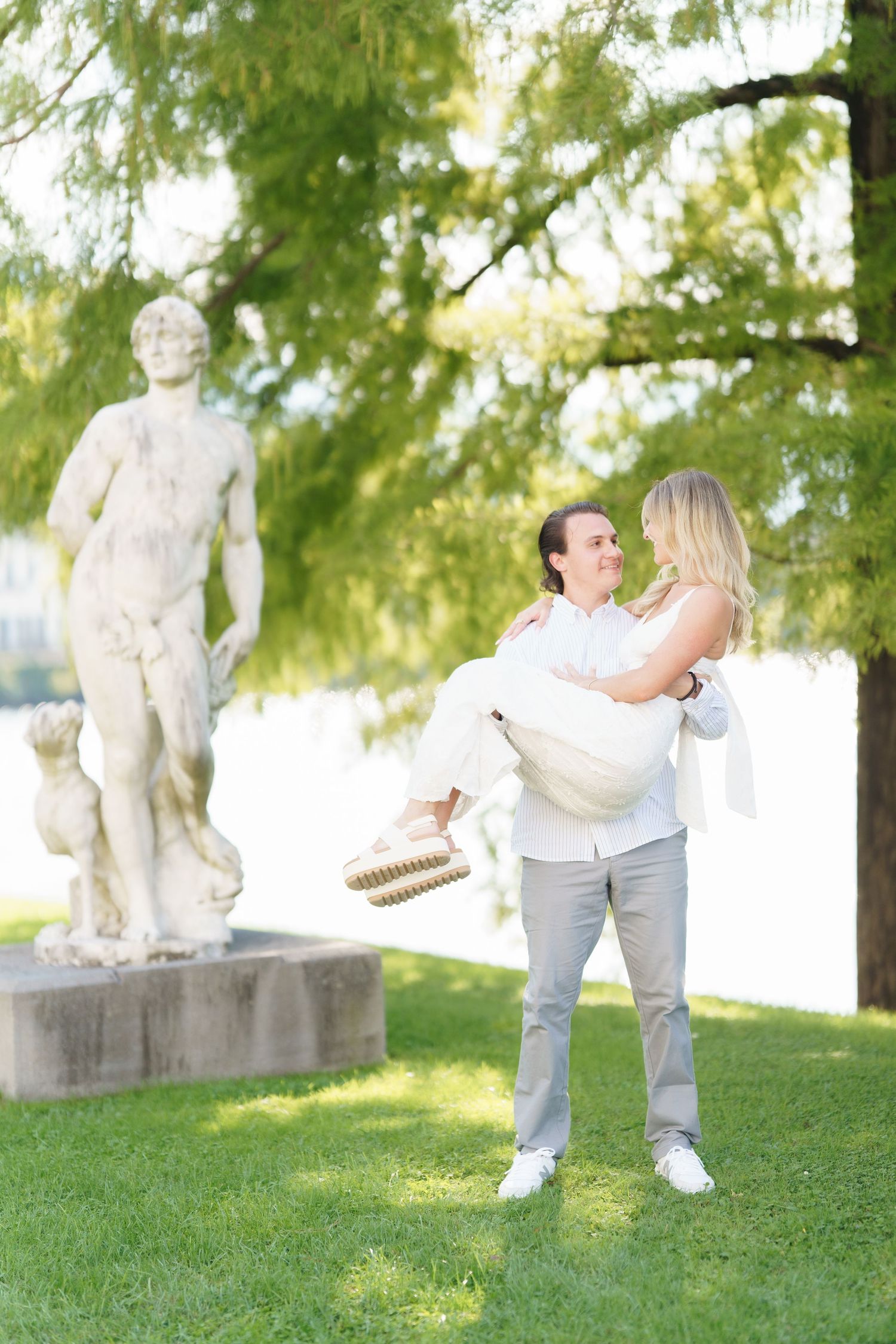 A romantic moment captured in a garden setting with a classical statue in the background on a sunny day.