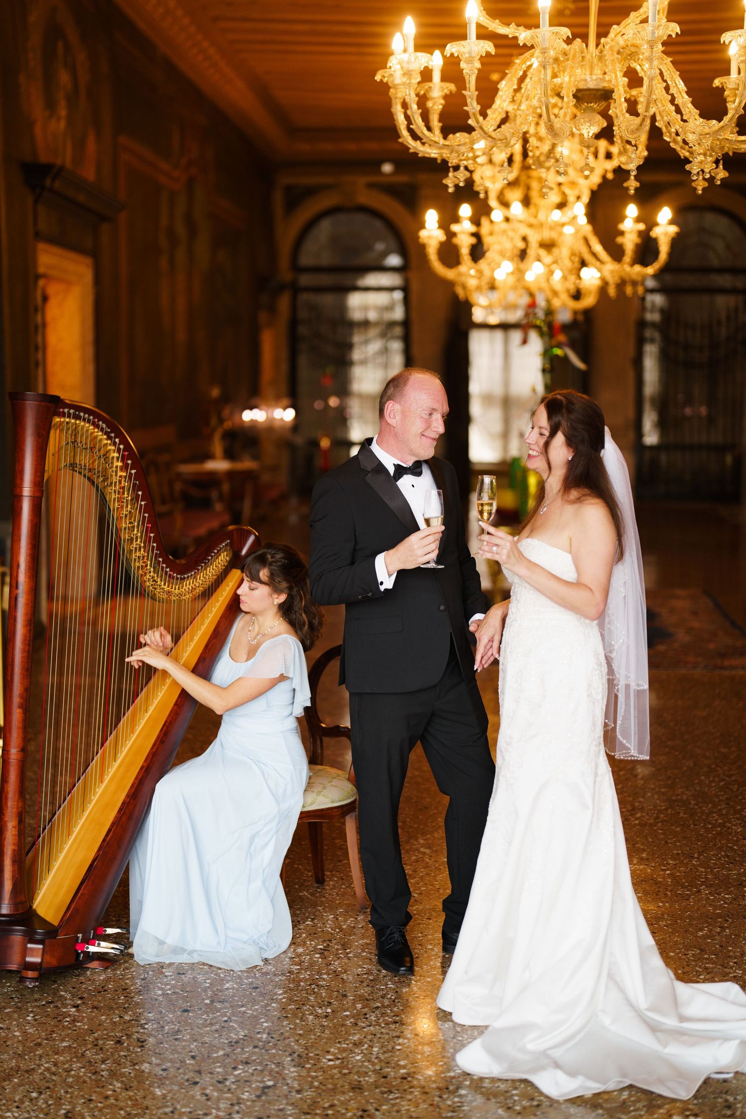 A wedding celebration in an elegant ballroom with a grand chandelier and harp player in a white dress.