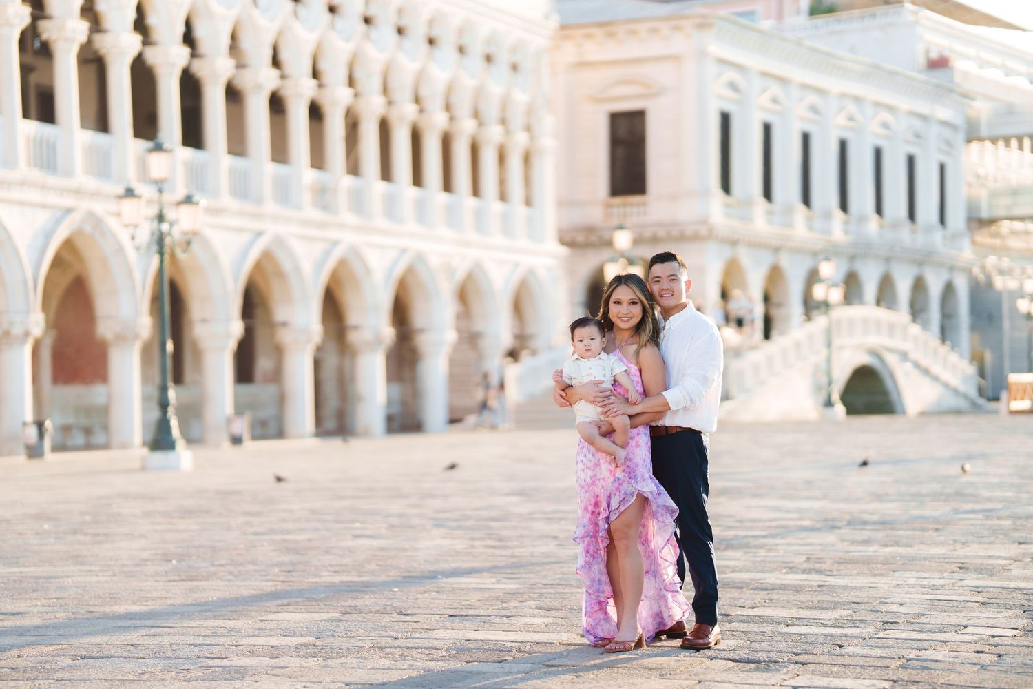Family posing together in St. Mark's Square Venice, with historic Doge's Palace arcade and bridge in background.