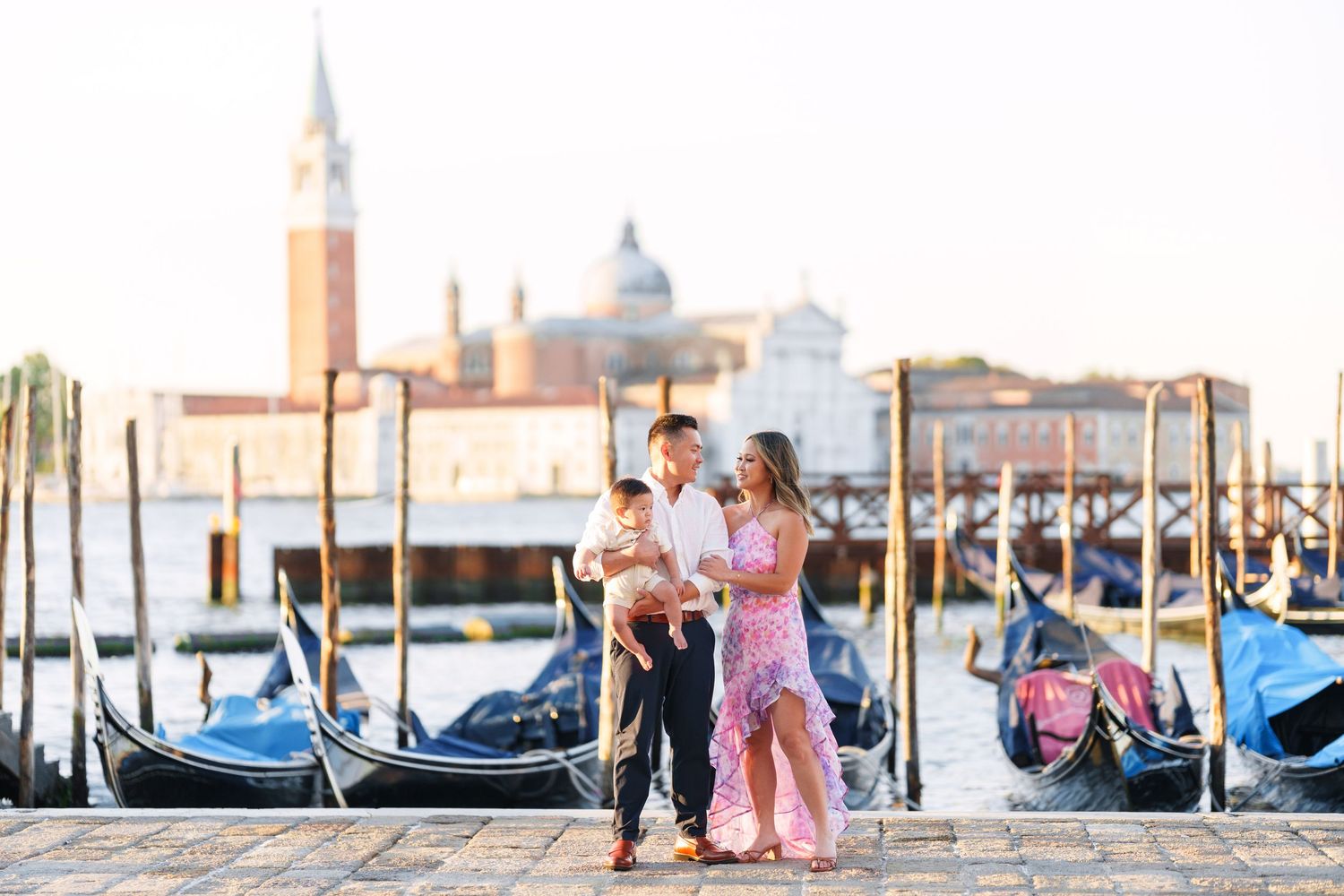Family with baby posing by gondolas on Venice Grand Canal with San Giorgio Maggiore church in background.