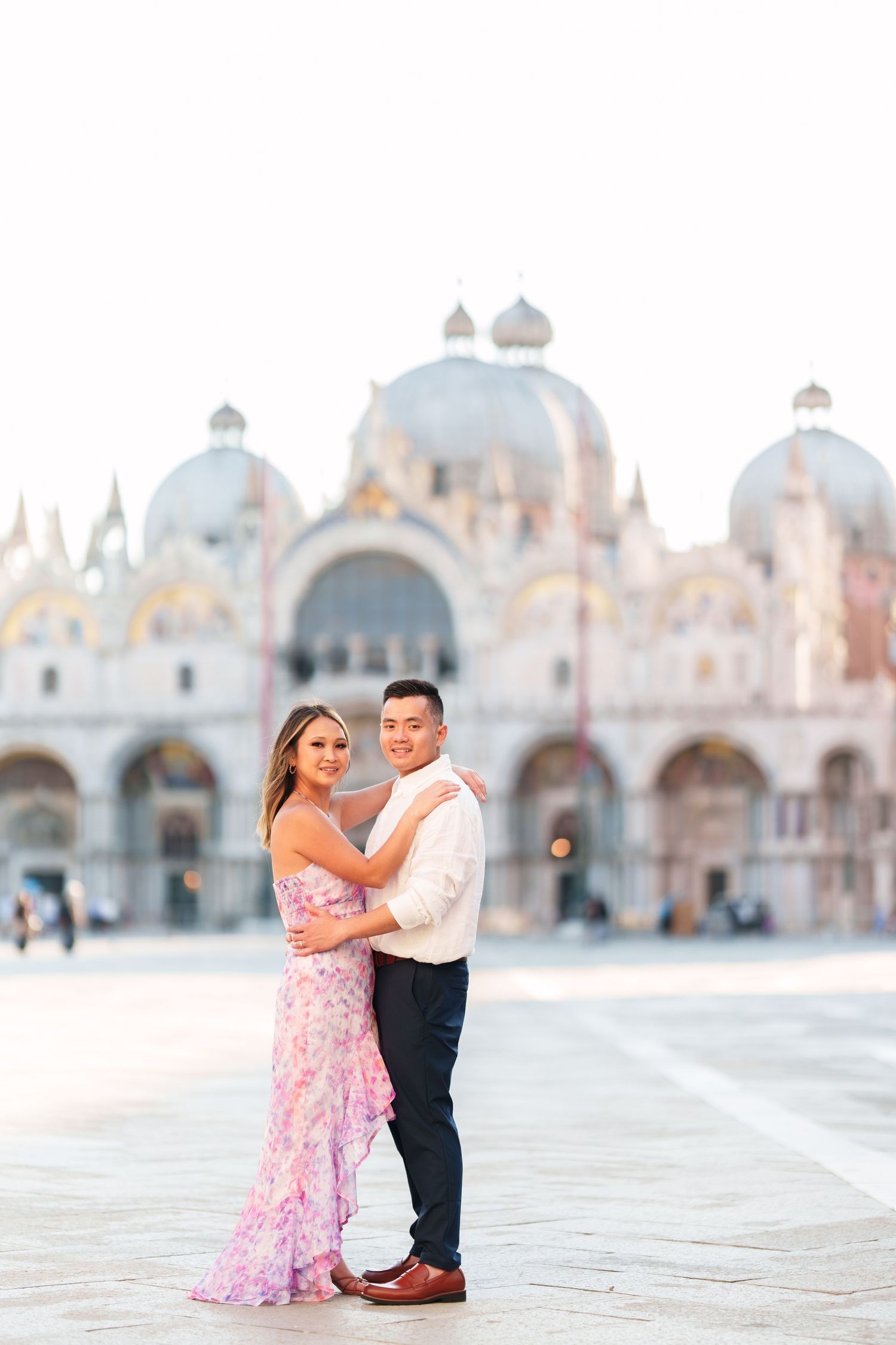 Couple embracing in St. Mark's Square, Venice, with the iconic Basilica di San Marco in the background.
