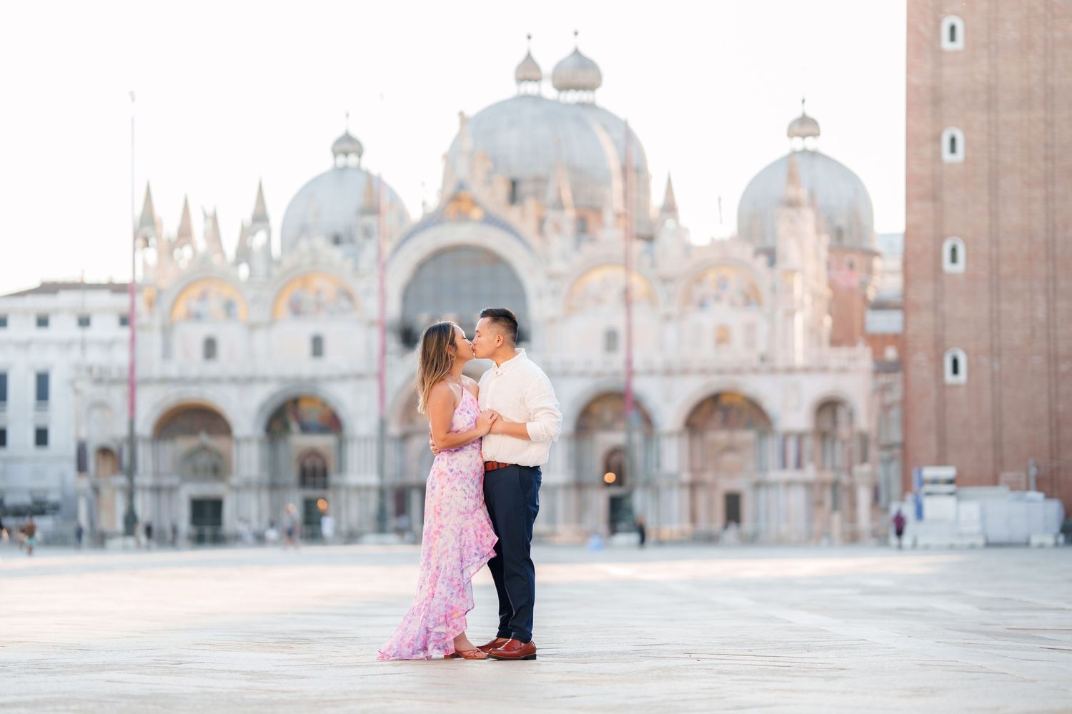Couple sharing a romantic kiss in St. Mark's Square with the iconic Basilica di San Marco in Venice, Italy.