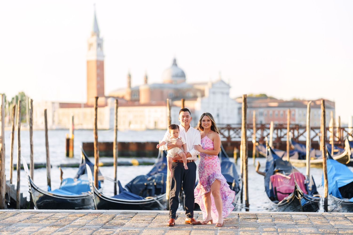 Family posing on Venice waterfront with gondolas and San Giorgio Maggiore church in background.