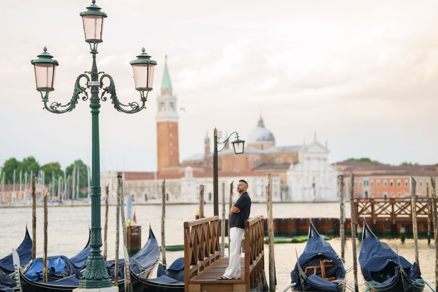 Woman standing by gondolas on Venice waterfront with San Giorgio Maggiore island in background.