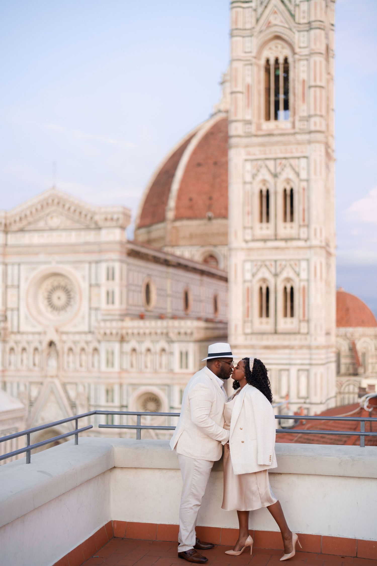Couple in white attire sharing a romantic moment on a rooftop terrace with Florence Cathedral backdrop.