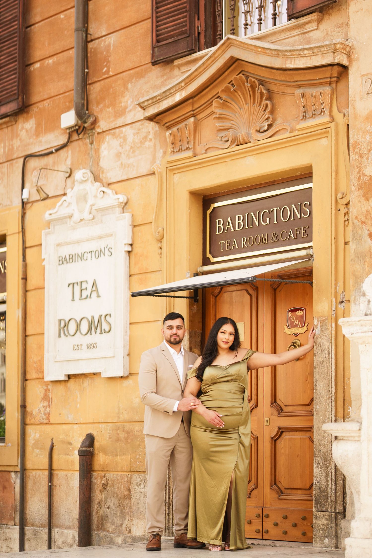 Couple poses in elegant attire outside Babingtons Tea Room and Cafe in Rome, Italy.