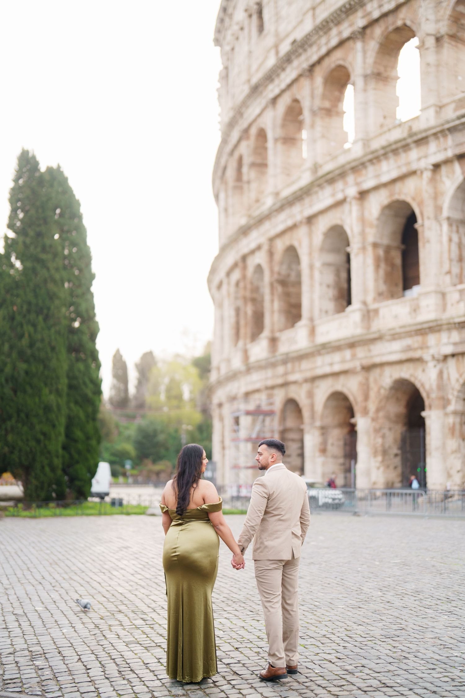Couple holding hands in front of the Colosseum in Rome, woman in green gown and man in beige suit.