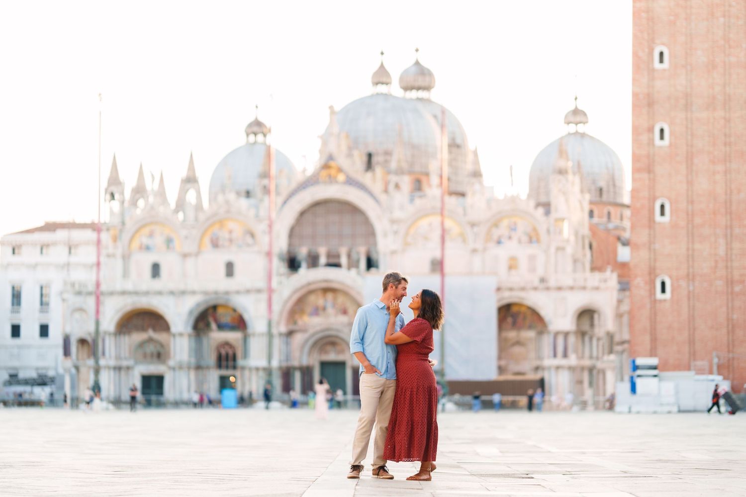 Couple embracing romantically in St. Mark's Square with the iconic Basilica di San Marco in Venice, Italy.