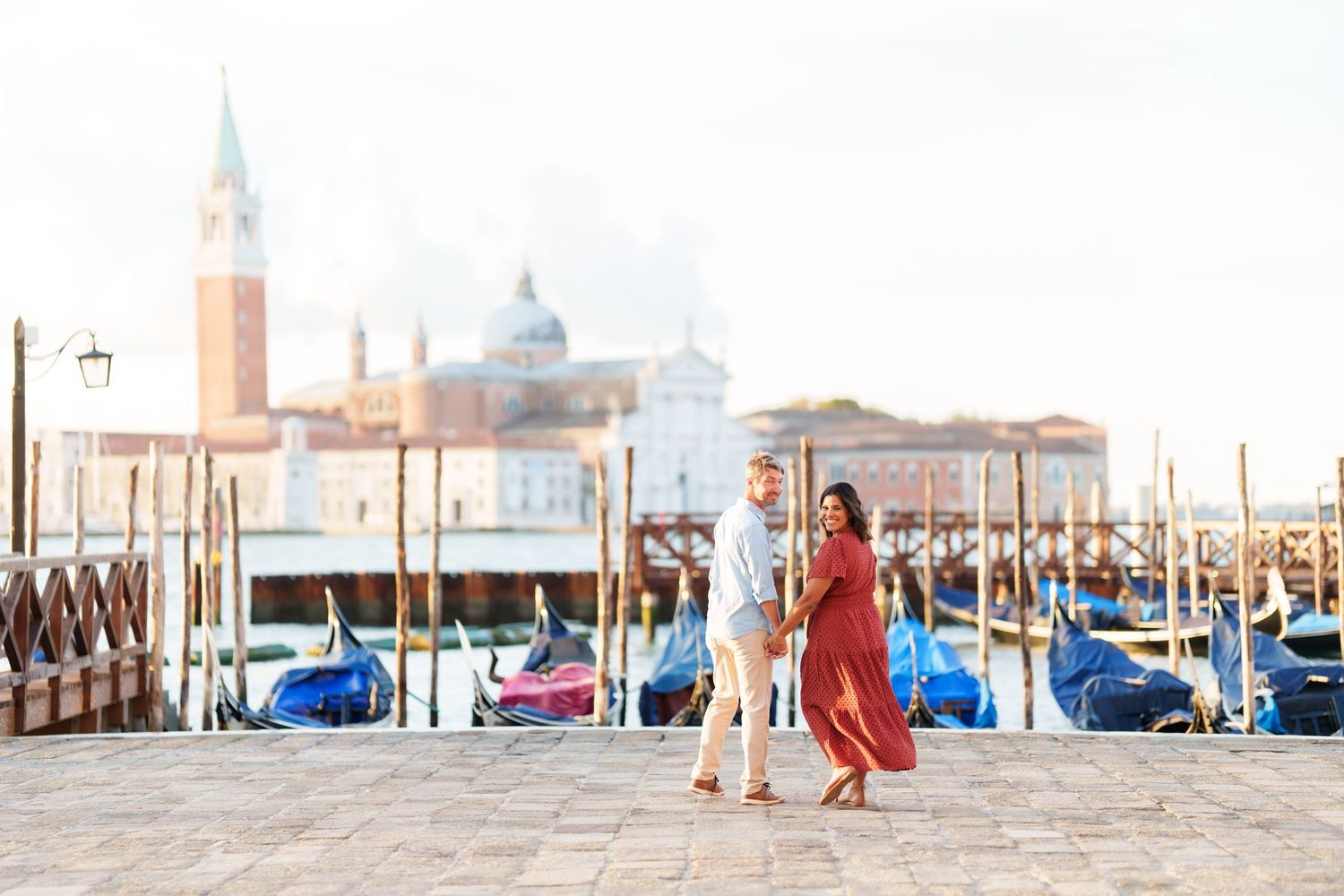 Couple dancing on Venice waterfront with gondolas and San Giorgio Maggiore church in soft morning light.