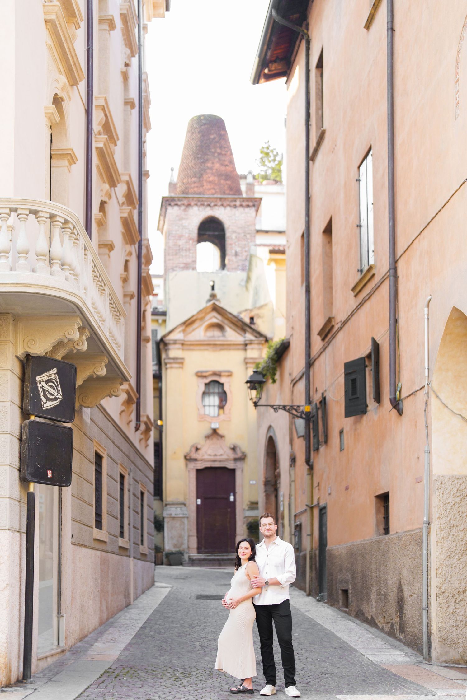 Romantic couple walks down a charming cobblestone street in a European town with historic architecture.
