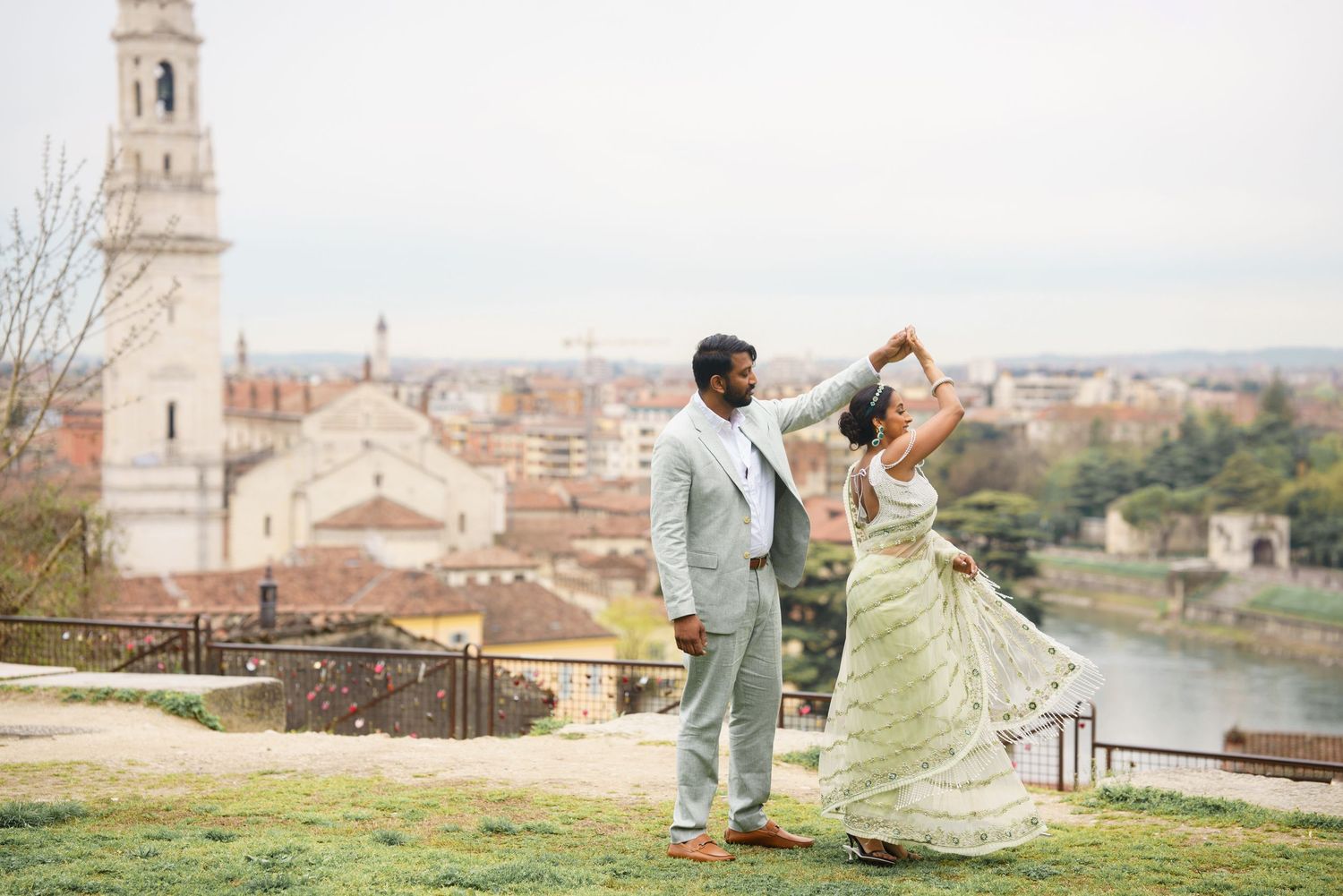 Couple dancing together on a scenic overlook with historic European city architecture and church tower in background.