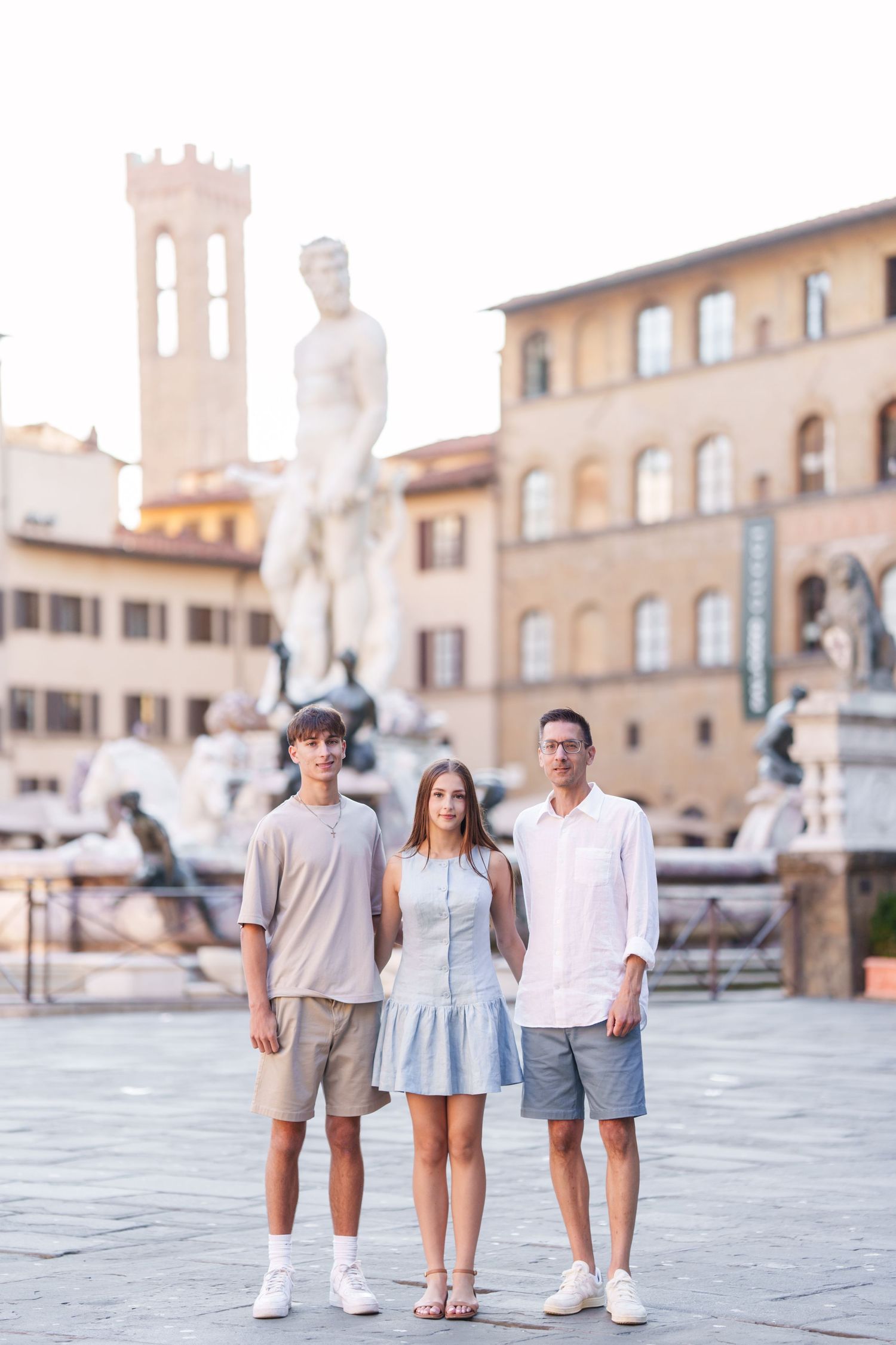 Family walking together in coordinated outfits through a historic Italian plaza with stone buildings in background.