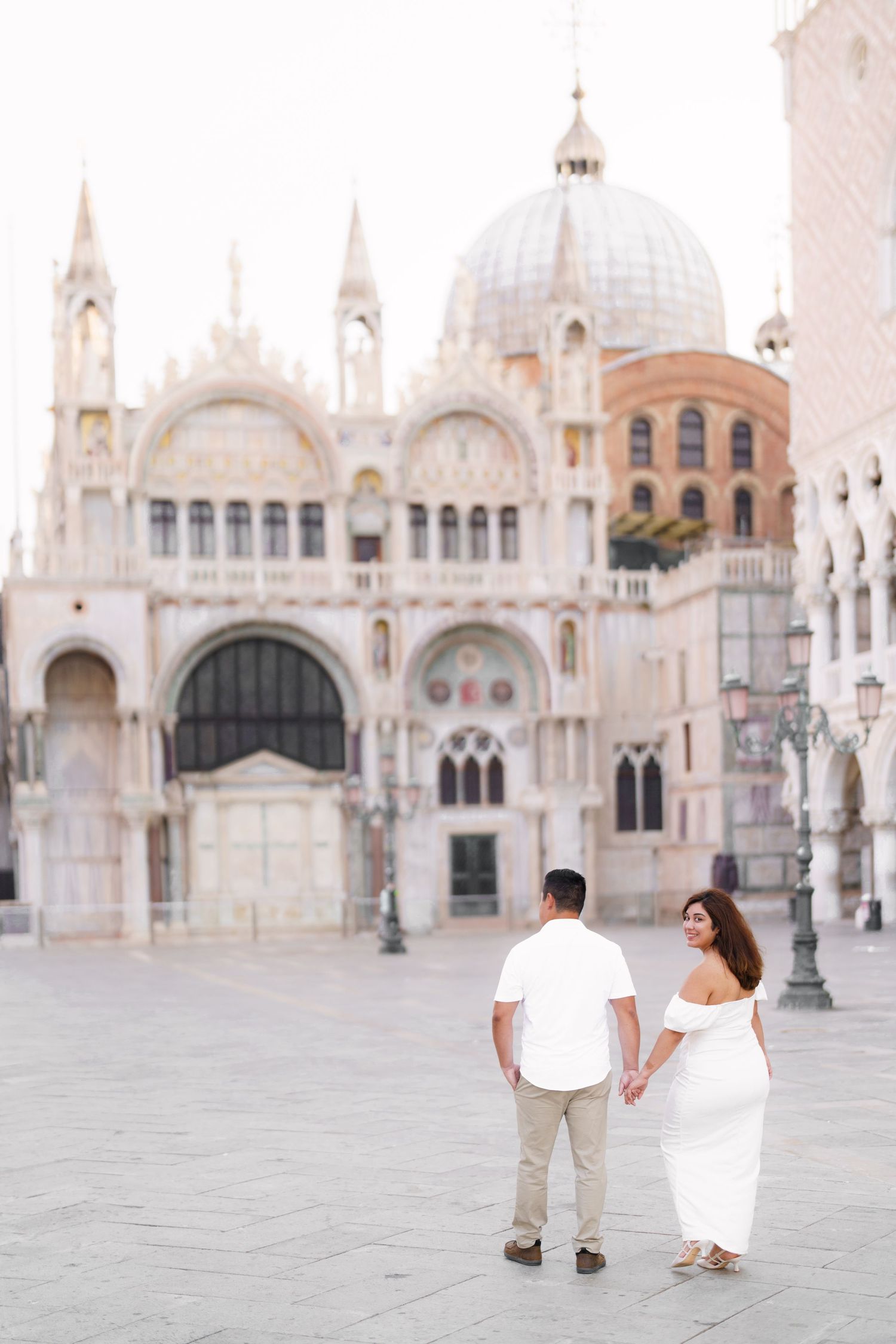 A couple shares a romantic moment in front of Saint Mark's Basilica in Venice's iconic Piazza San Marco.