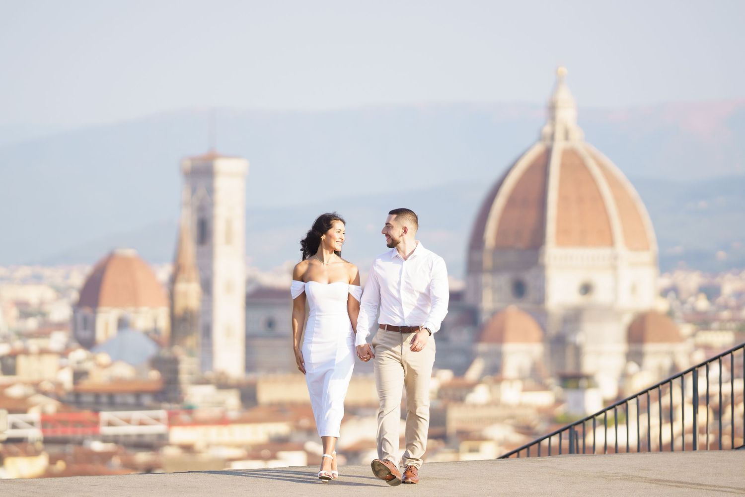 Couple walking on terrace overlooking Florence skyline with iconic Duomo cathedral dome in background.