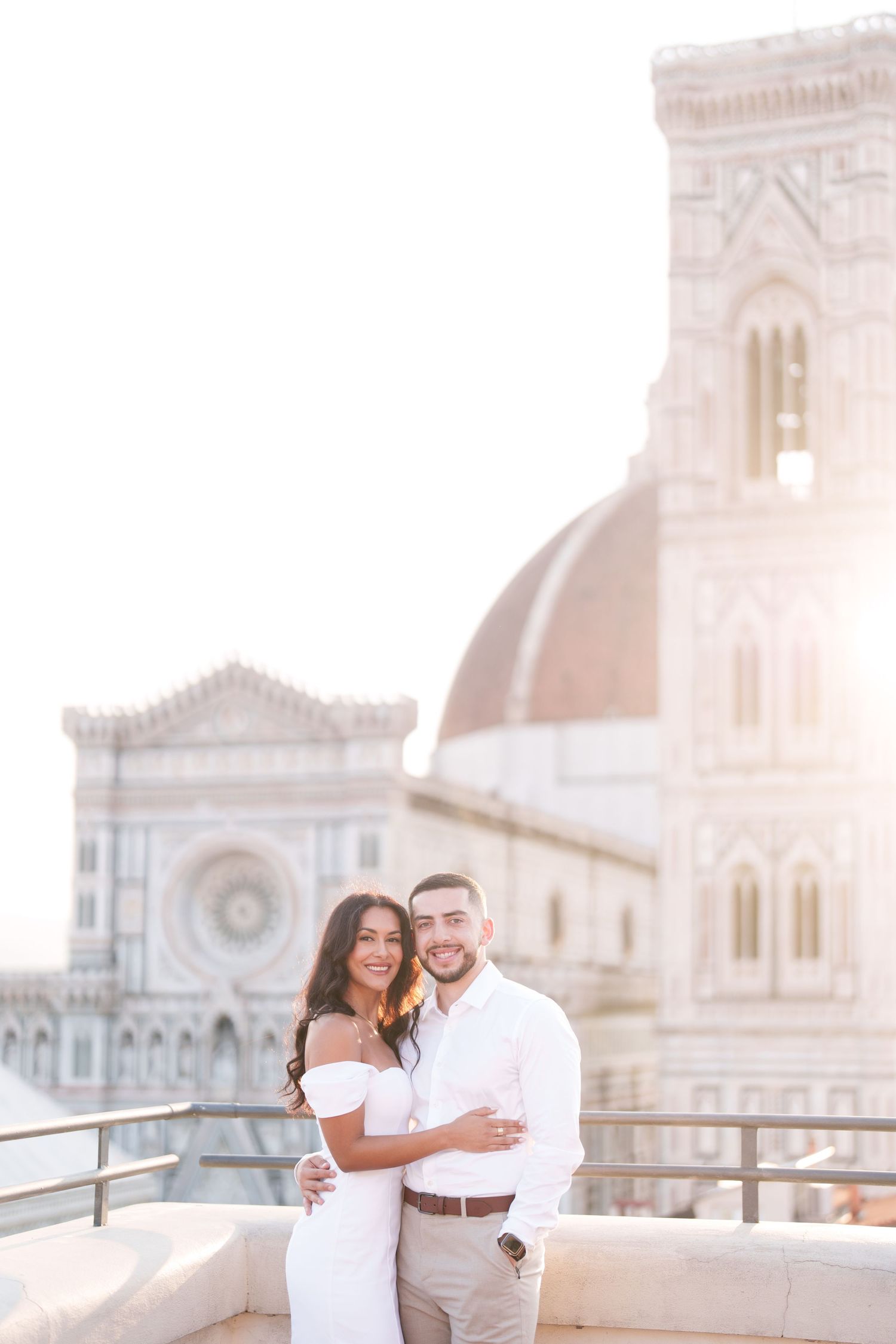 A couple embraces while posing together on a balcony overlooking Florence Cathedral in Italy during sunset.